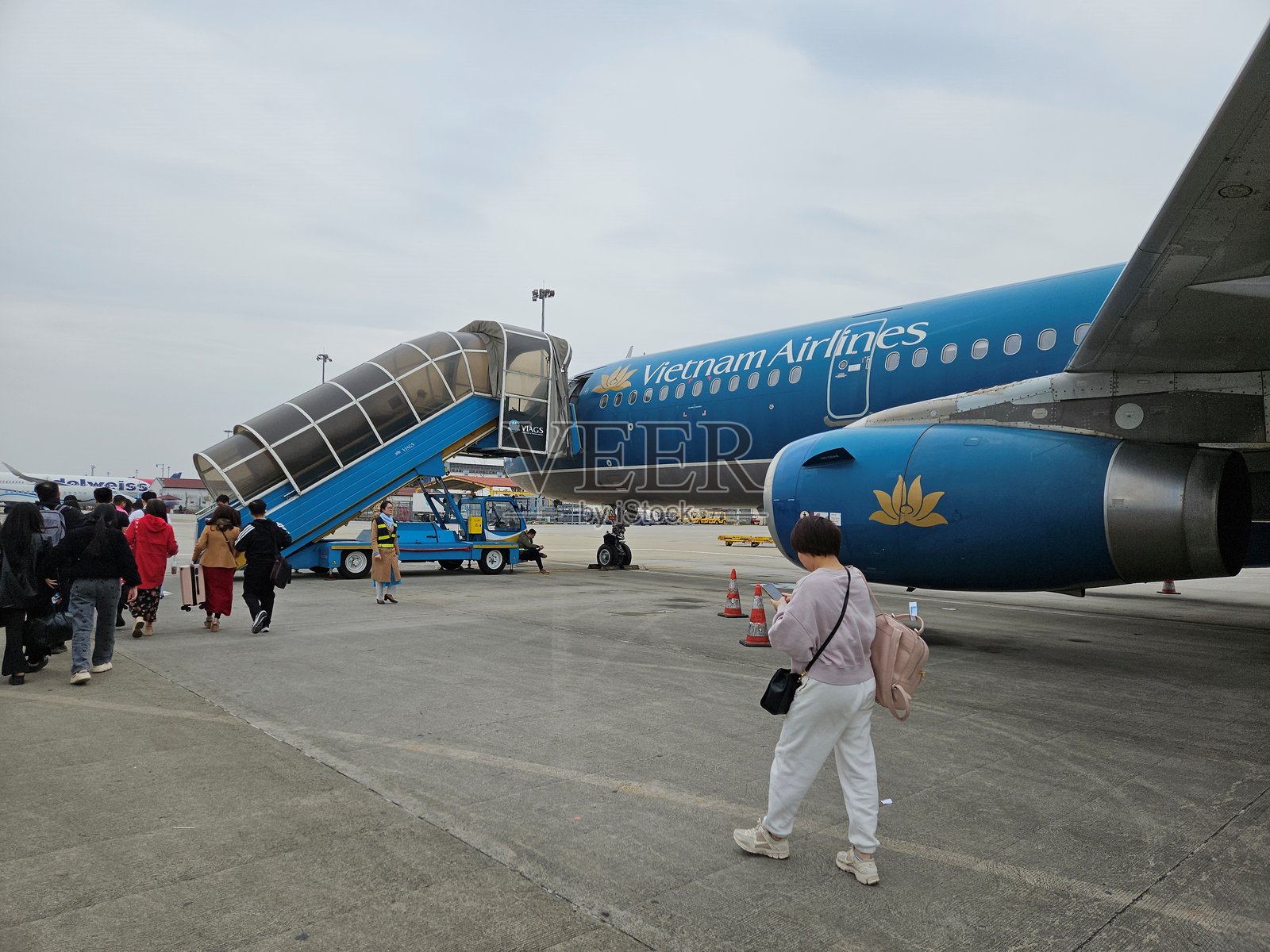 乘客们正在通过移动楼梯在内排机场的停机坪上登上蓝色飞机。照片摄影图片