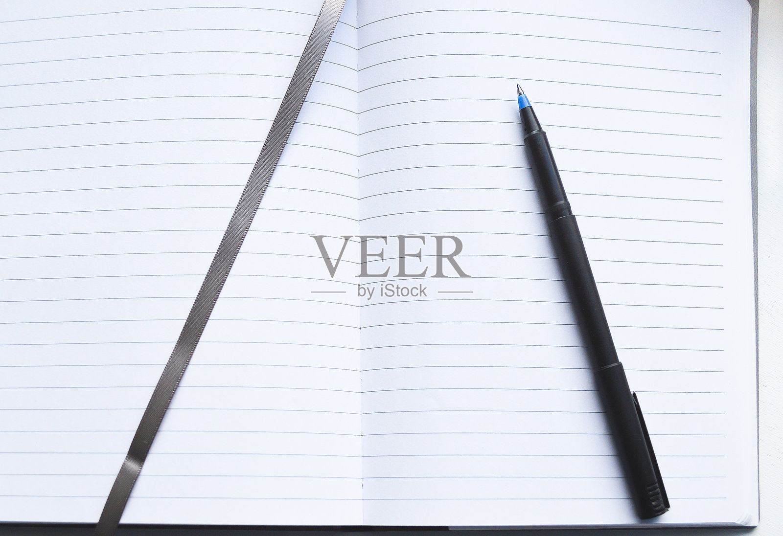 一本打开的有横线页的笔记本上放着一支黑色钢笔和一条灰色丝带书签照片摄影图片
