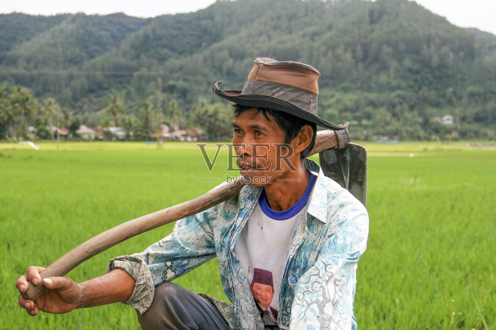 一位当地印尼稻田农民在印尼西苏门答腊的哈劳谷里扛着锄头。照片摄影图片
