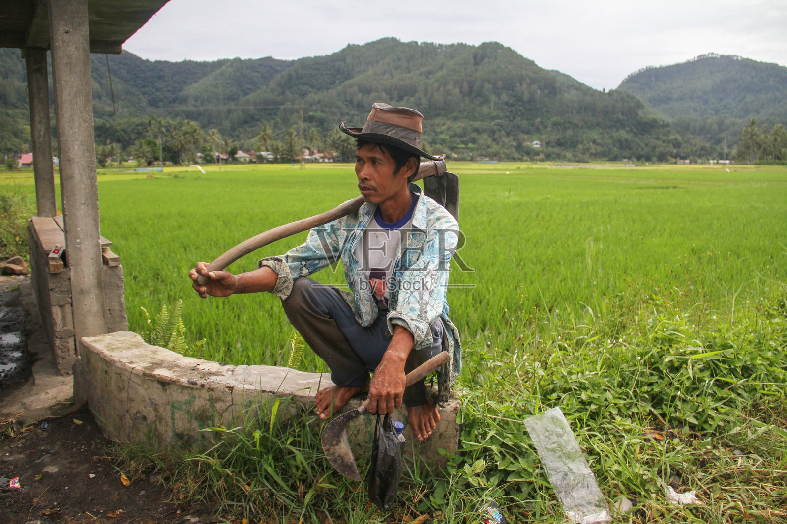一位当地印尼稻田农民在印尼西苏门答腊的哈劳谷里扛着锄头。照片摄影图片