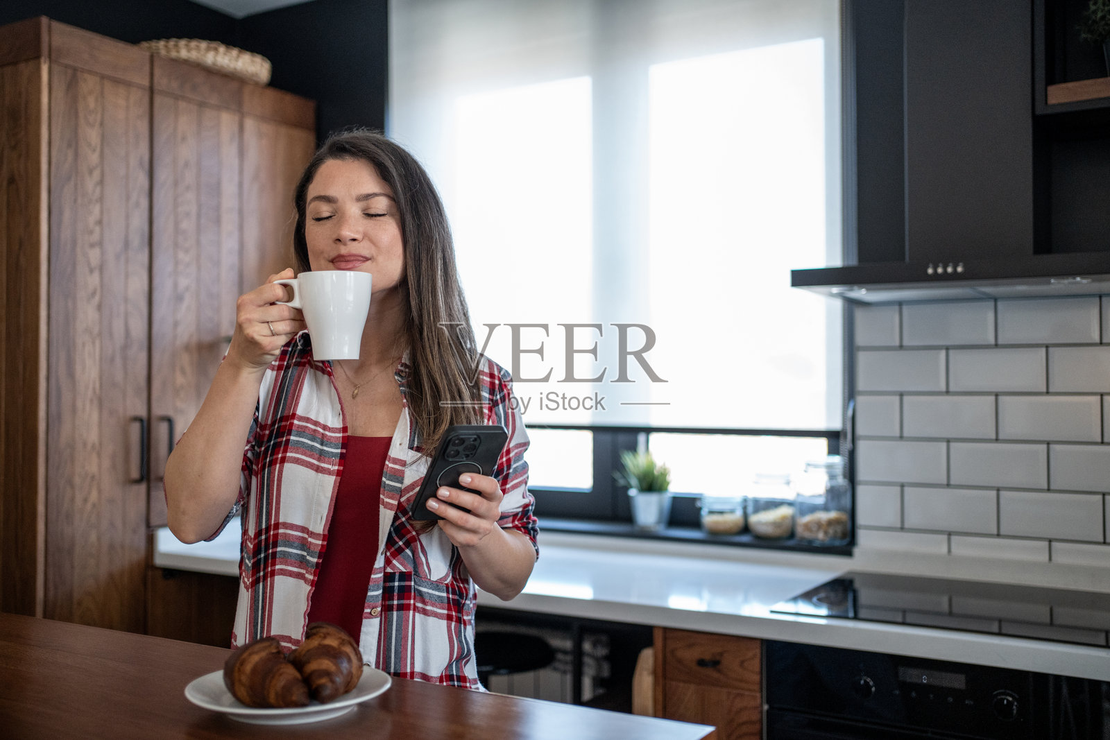 女性在现代厨房中享受咖啡并使用智能手机照片摄影图片