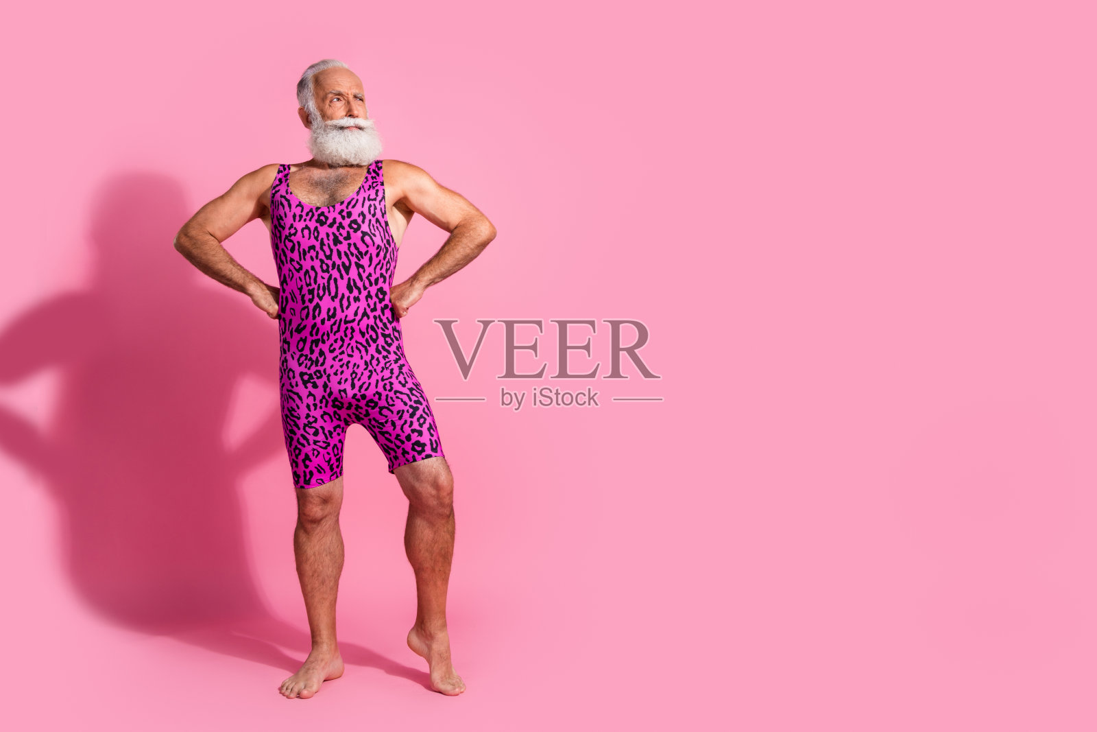 强壮的肌肉老年男性穿着女性服装，接受自我，背景为粉色。照片摄影图片