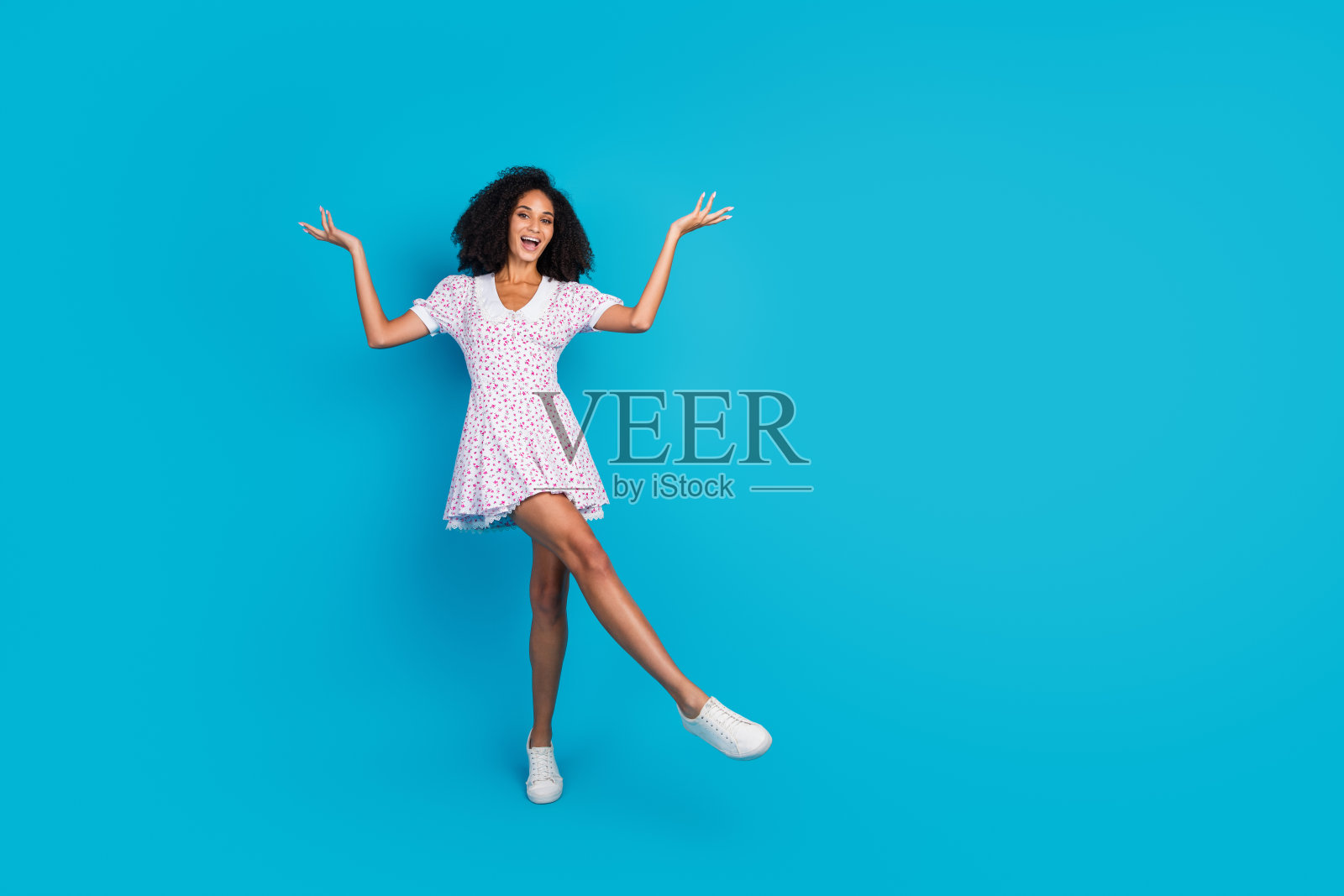 年轻时尚女性穿着印花裙，站在鲜艳的蓝色背景前，展现出快乐与美丽。照片摄影图片