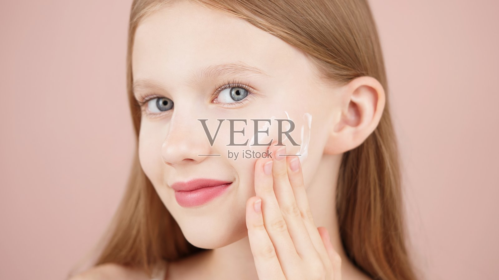 微笑的快乐女孩在脸颊上涂抹面霜以使肌肤焕发光彩照片摄影图片