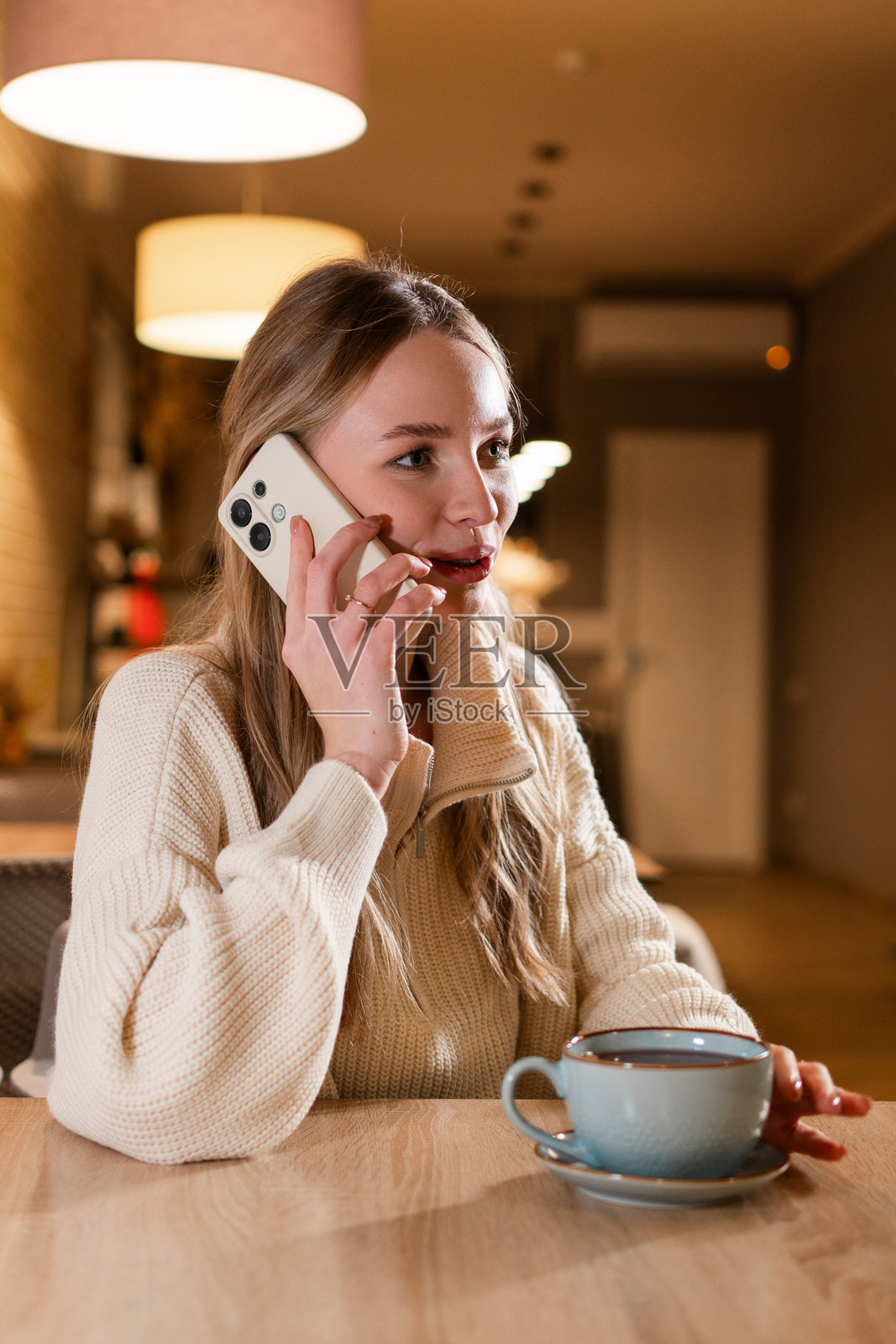 微笑的年轻女性坐在咖啡馆里用手机交谈。迷人的女孩在咖啡店里轻松地与朋友通话，笑得很开心。照片摄影图片