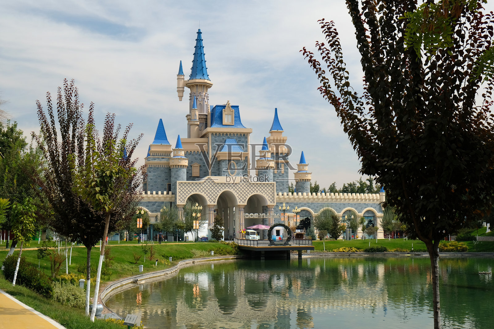 宏伟的城堡与蓝色塔楼在阳光明媚的下午映照在公园湖泊的宁静水面上照片摄影图片