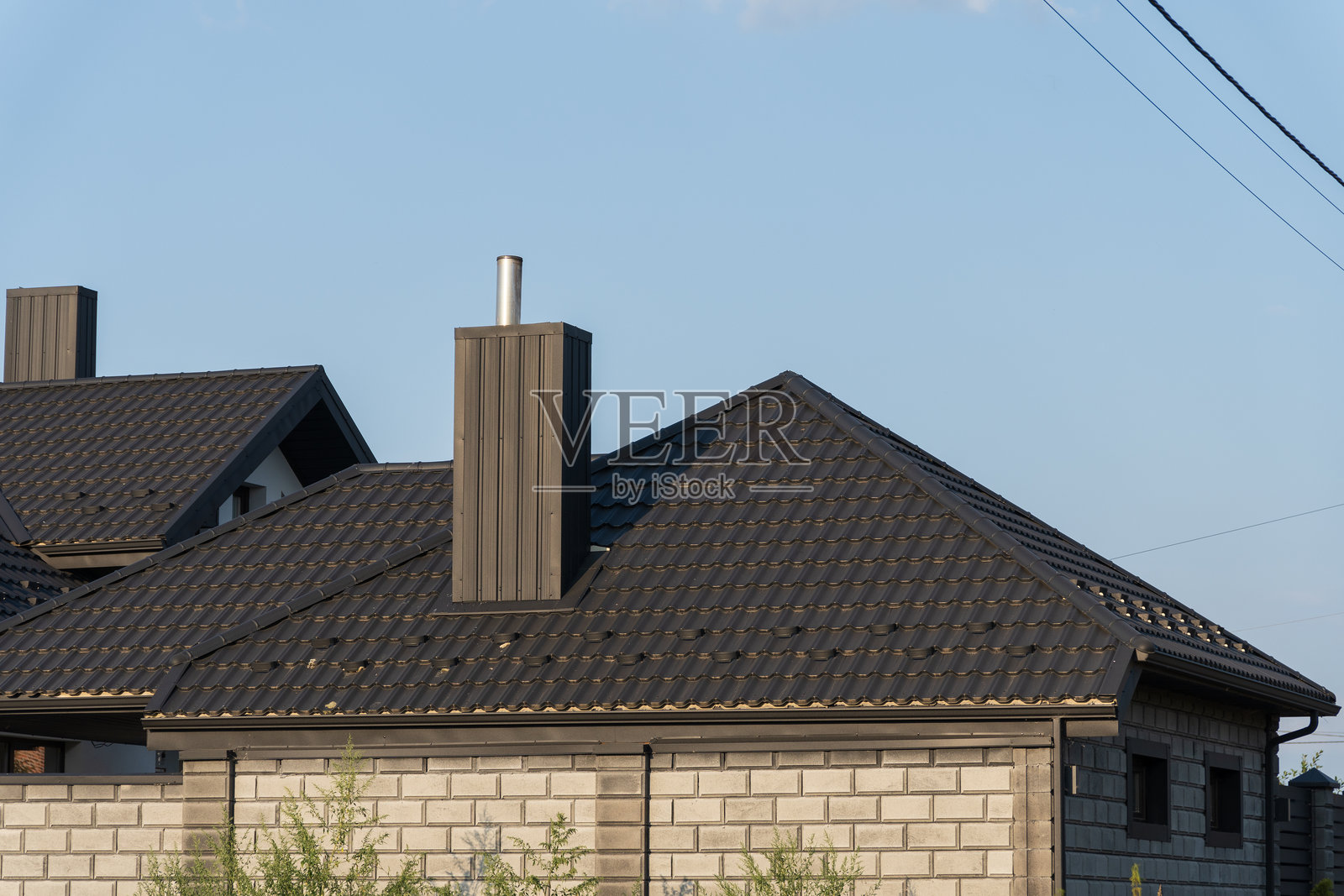 两座现代住宅展示了深色瓷砖屋顶、金属装饰和天窗，在晴朗的蓝天下，突显了现代建筑风格。照片摄影图片