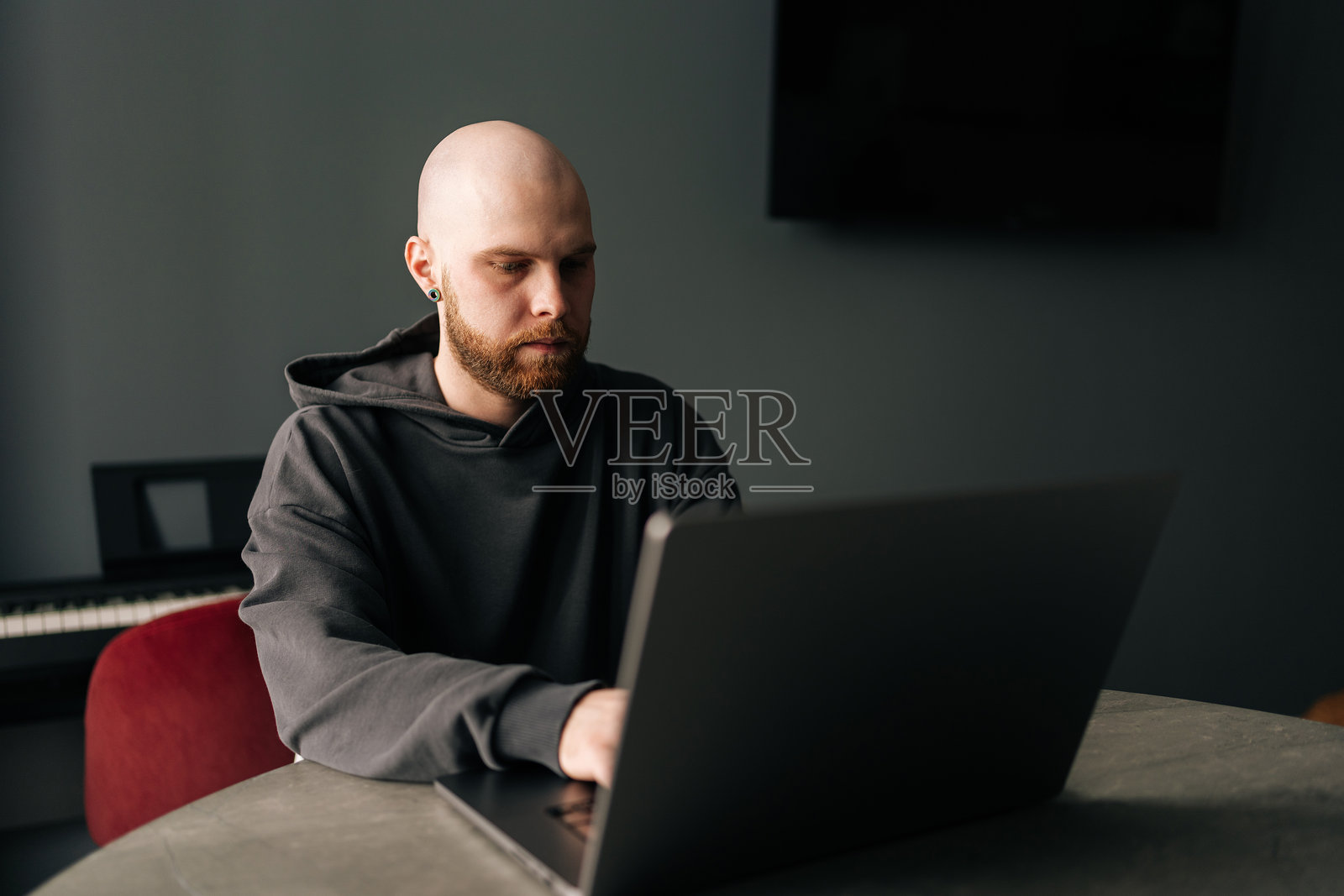 专注的男性程序员，留着胡子，穿着连帽衫，在家远程工作，坐在桌子前，专心致志地在笔记本电脑上打字。照片摄影图片