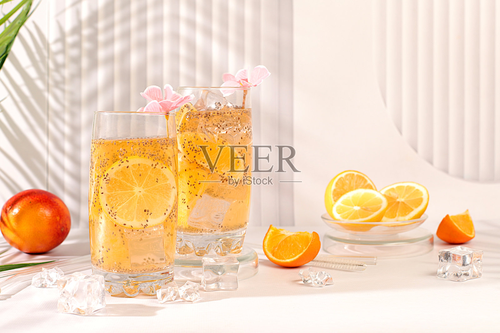 现代静物画，包含柑橘类水果。素食鸡尾酒，配有奇亚籽、橙子、青柠、紫色花朵和冰块。排毒饮食和减肥概念。夏季横幅和屏幕模板。照片摄影图片