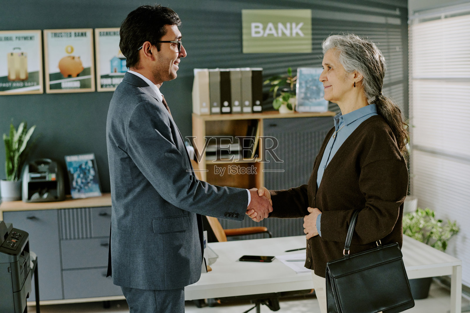 商人在办公室与一位年长的西班牙裔女性握手照片摄影图片