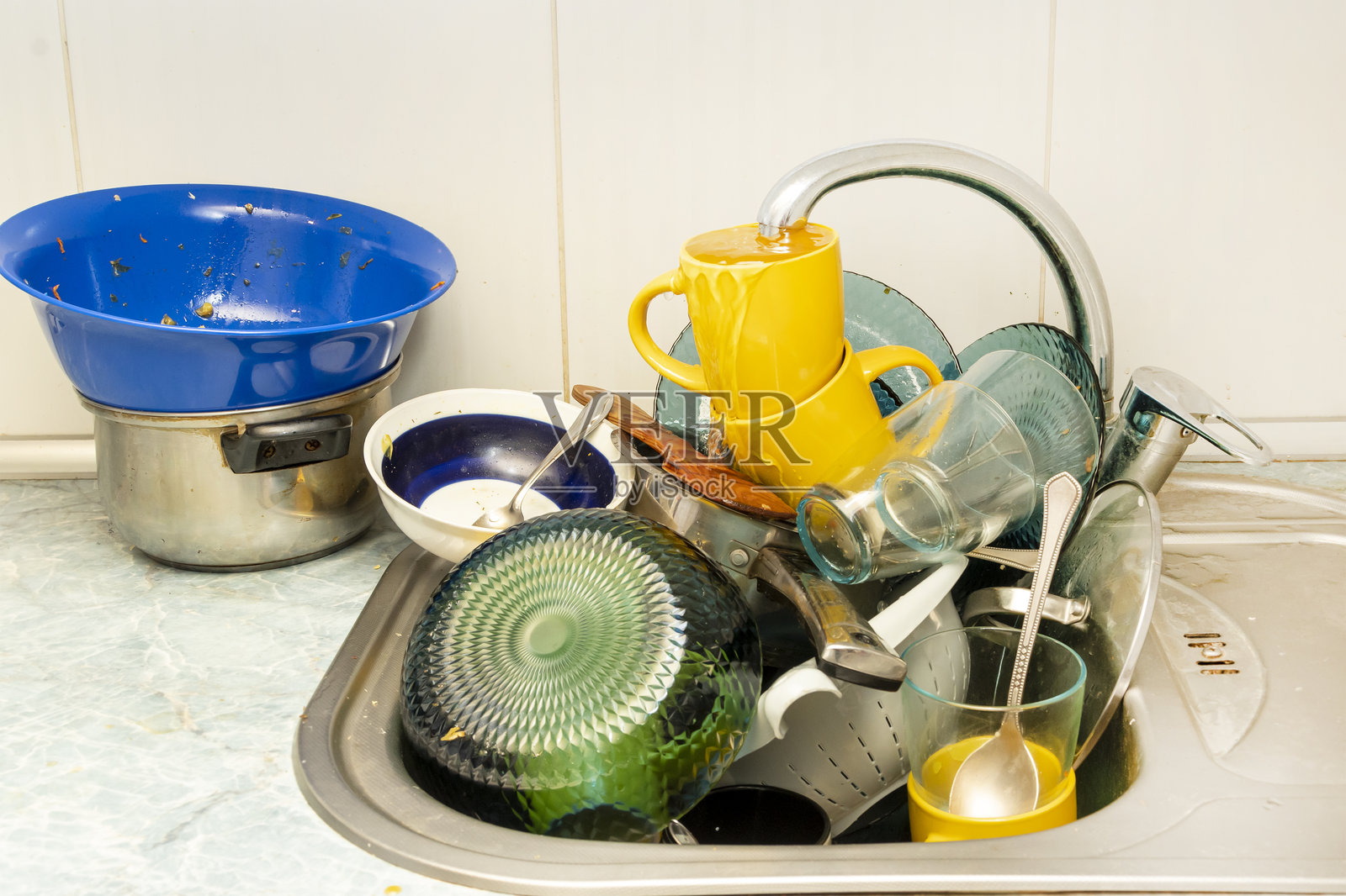 肮脏且未清洗的餐具堆积在厨房水槽中。未清洗的杯子、盘子、锅、叉子和勺子。杂乱无章的脏餐具如山般堆积。照片摄影图片