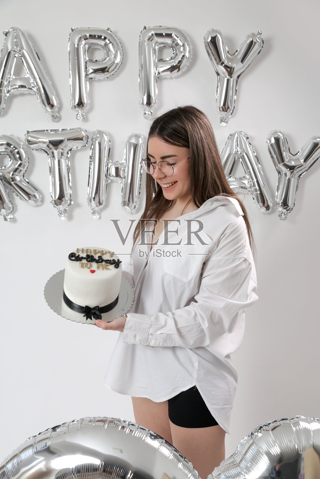 生日摄影棚拍摄。年轻的白人女孩在白色背景下与氦气球拍照。照片摄影图片