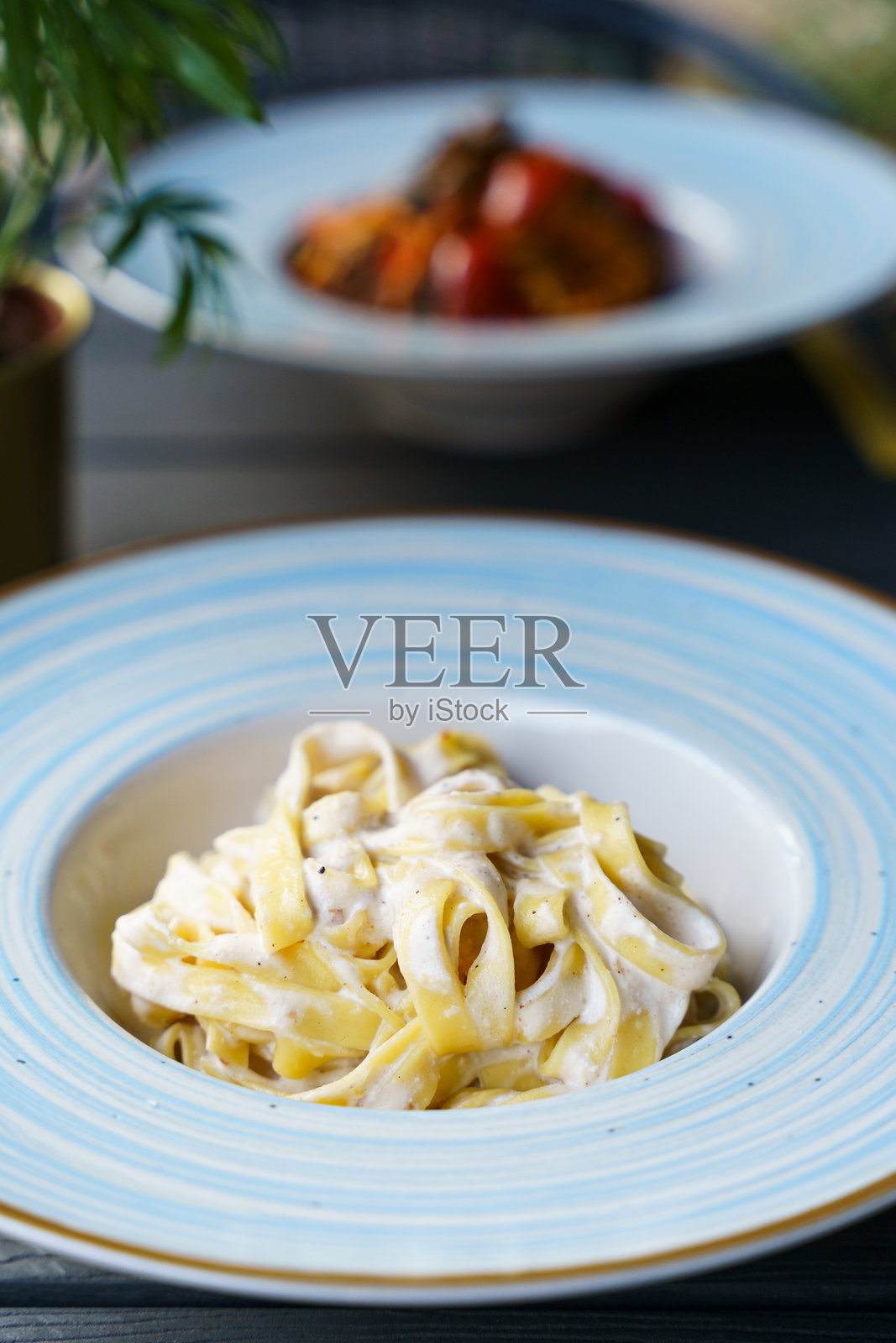 奶油意大利宽面条阿尔弗雷多，盛在蓝条纹盘子上照片摄影图片