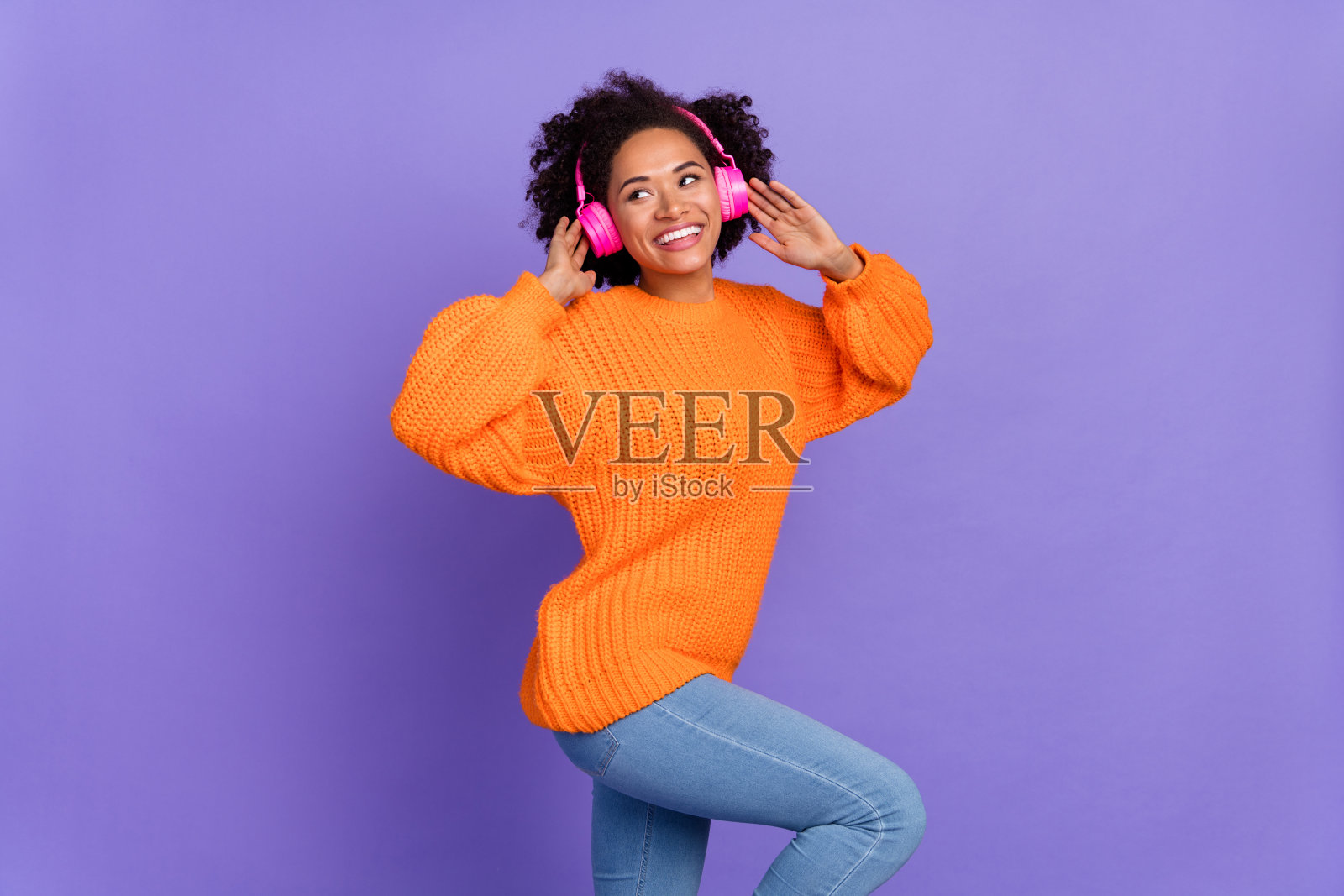 迷人的女孩在明亮的紫色背景下，愉快地跳舞，享受立体声旋律的热曲。照片摄影图片