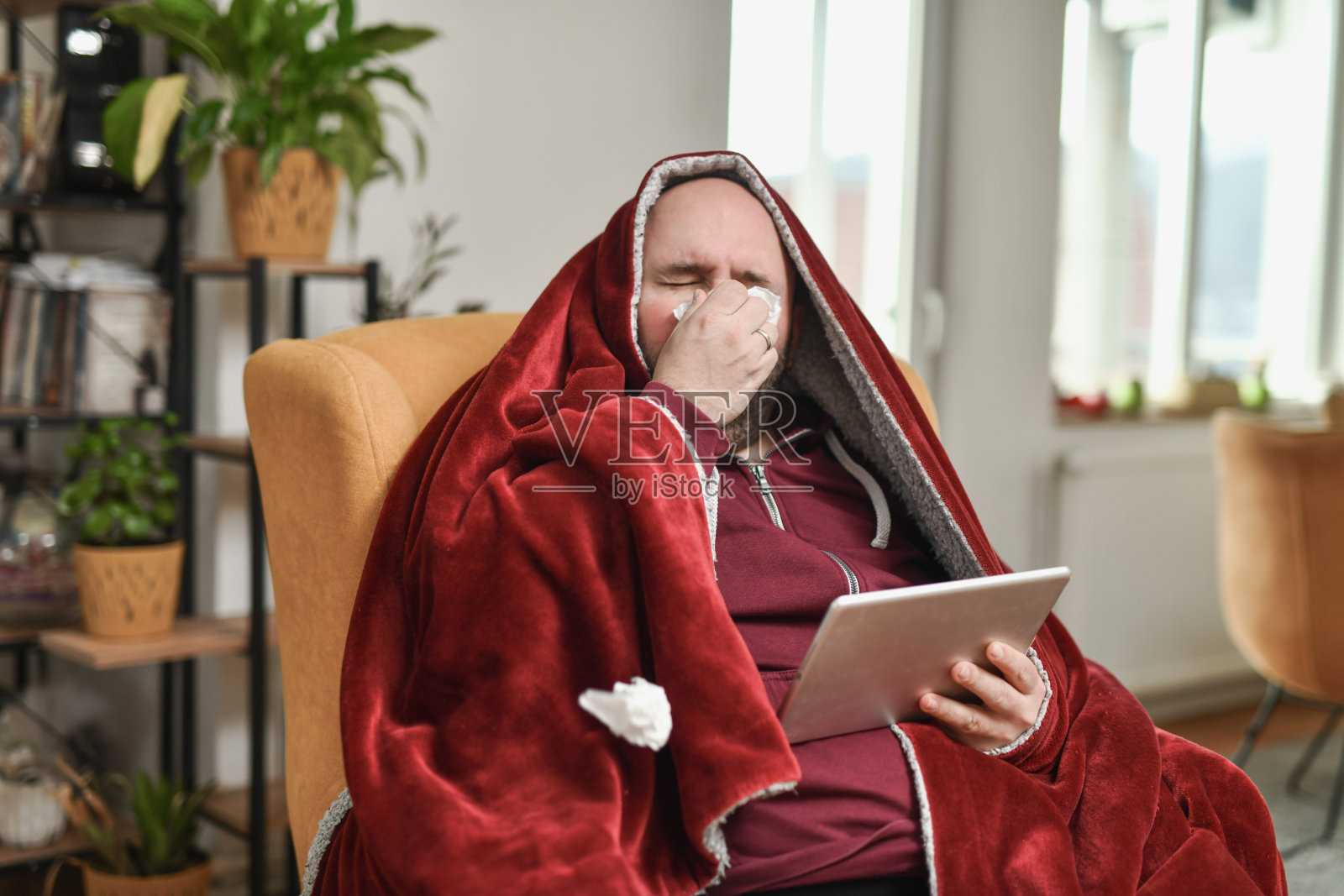 男性擦拭流鼻涕，发烧感冒，正在观看数字平板上的电视节目照片摄影图片