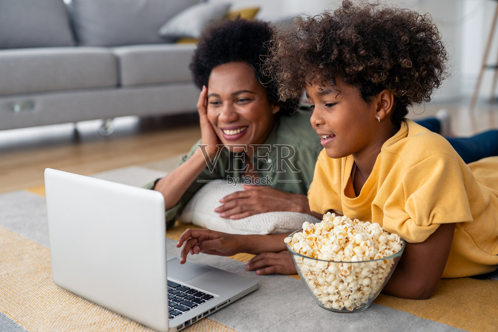 快乐的非洲母女在家中放松，享受着笔记本电脑和爆米花。照片摄影图片