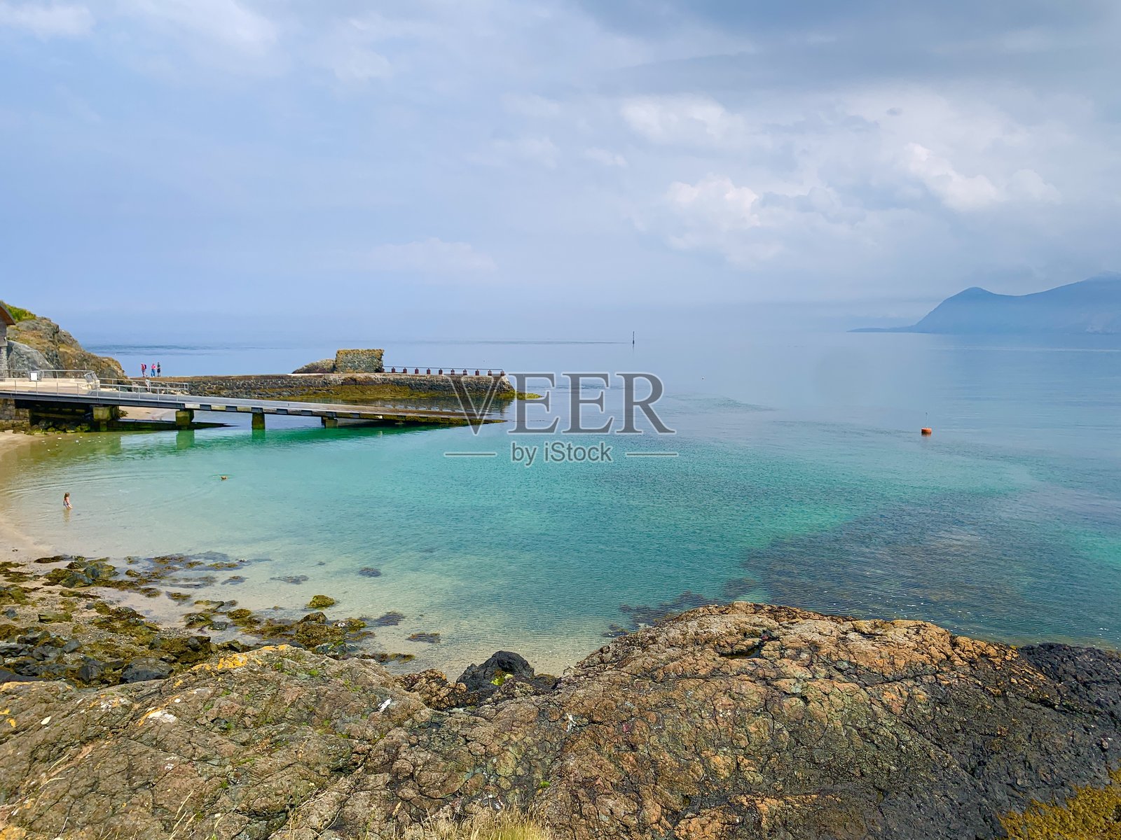 岩石海滩，带有船坡和山脉背景的小海湾照片摄影图片