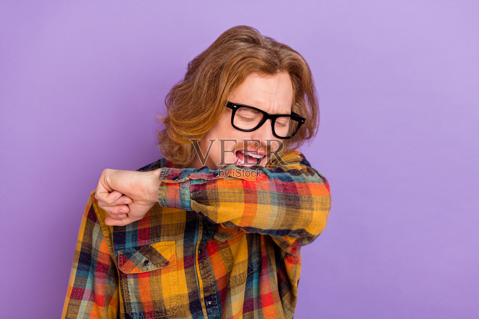 吸引人的生病男子在鲜艳的紫色背景下打喷嚏，显得痛苦。照片摄影图片