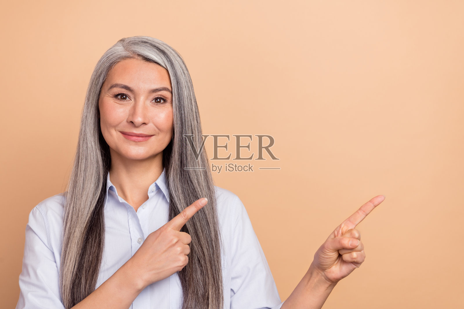 成熟的女性用手指指向空白区域，选择横幅，背景为米色。照片摄影图片