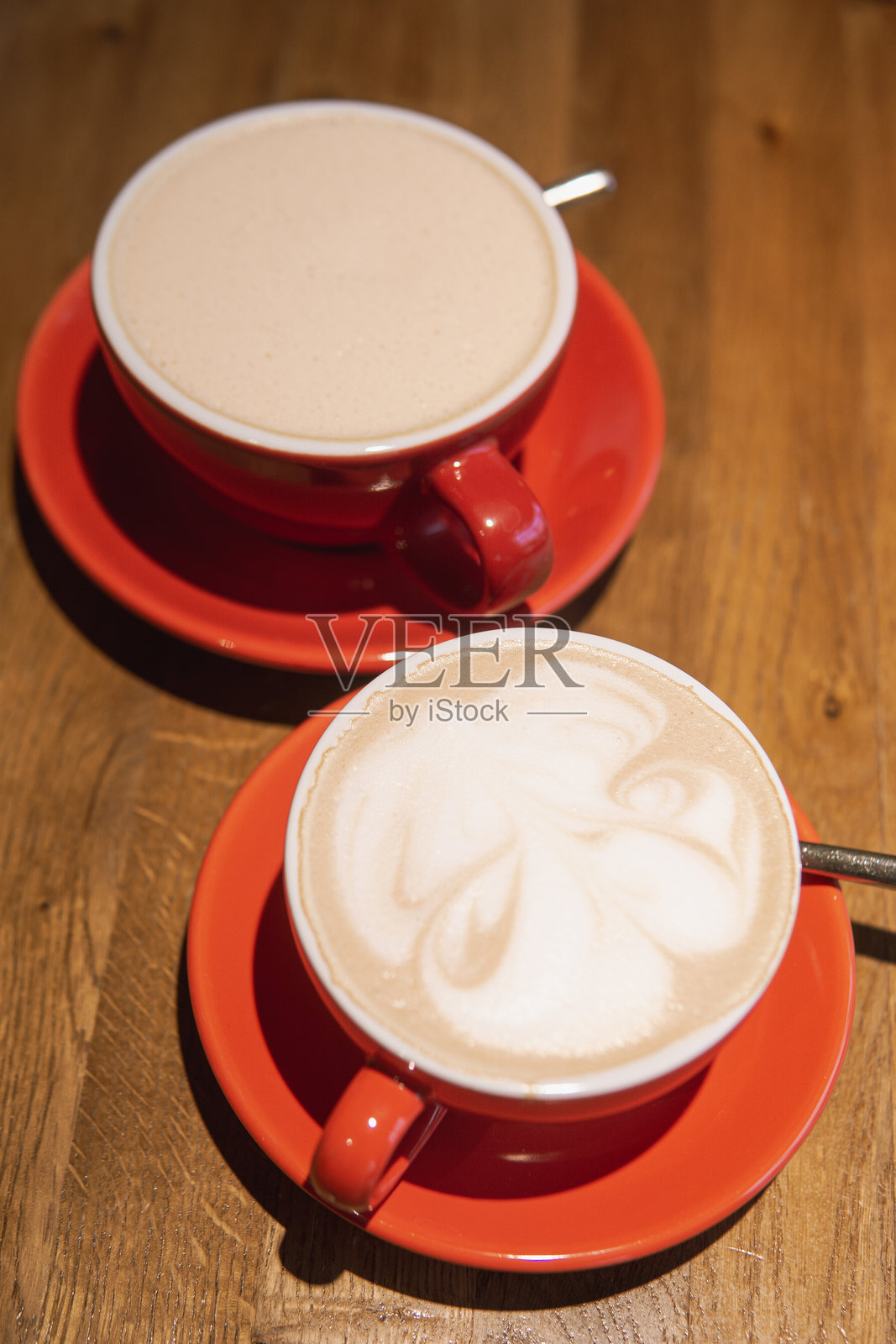 鲜艳红色陶瓷杯中的咖啡，杯面有精致的图案，静静地放在光滑的木桌上，散发出温暖的气息，邀请分享的时刻。照片摄影图片