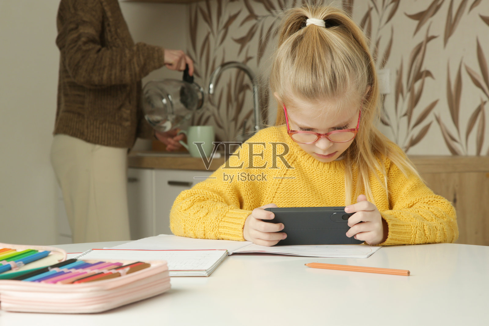 小女孩在厨房桌子上做作业时使用手机照片摄影图片
