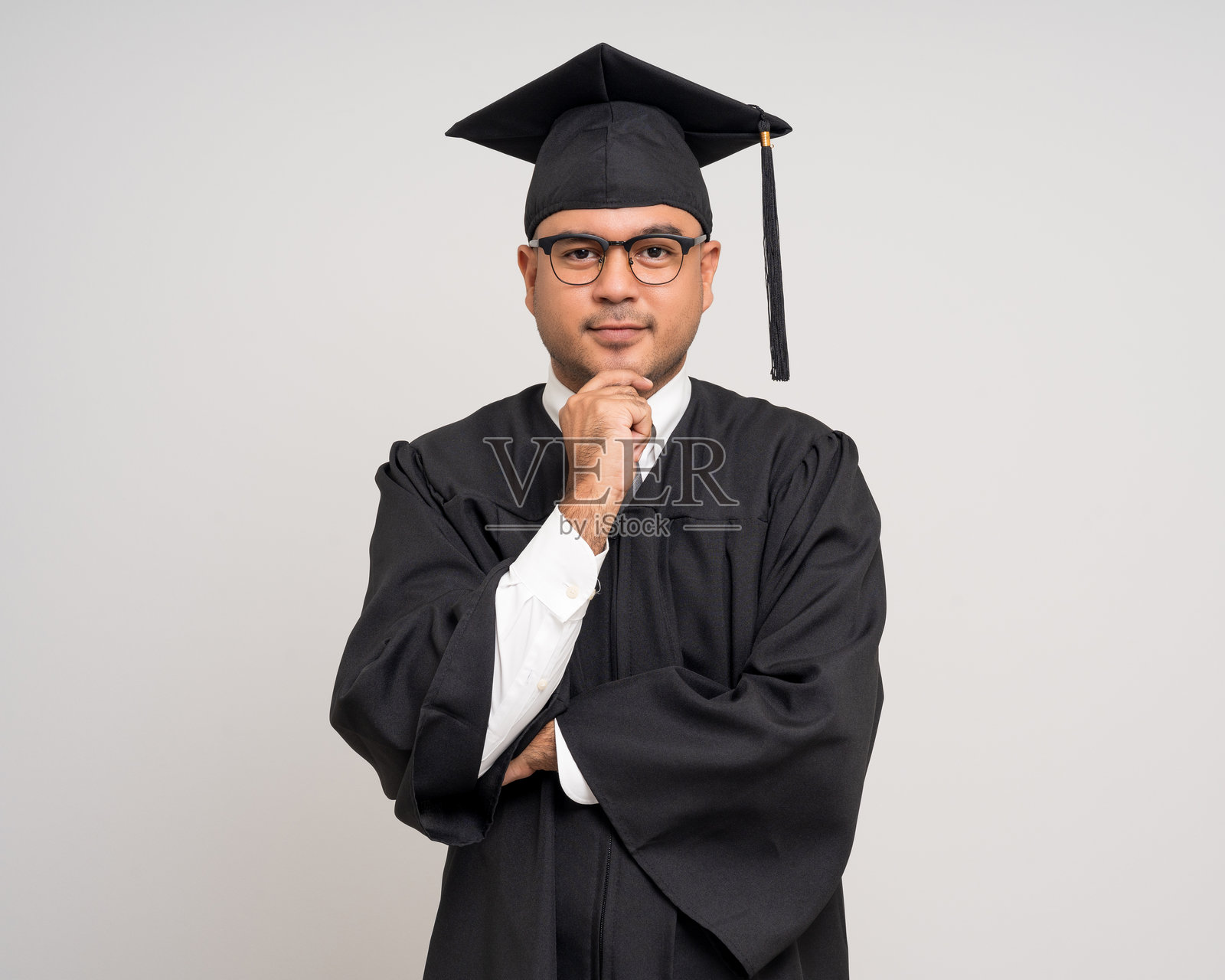 思考的年轻亚洲男子穿着毕业服和学位帽，背景为单色。大学学位教育毕业。照片摄影图片