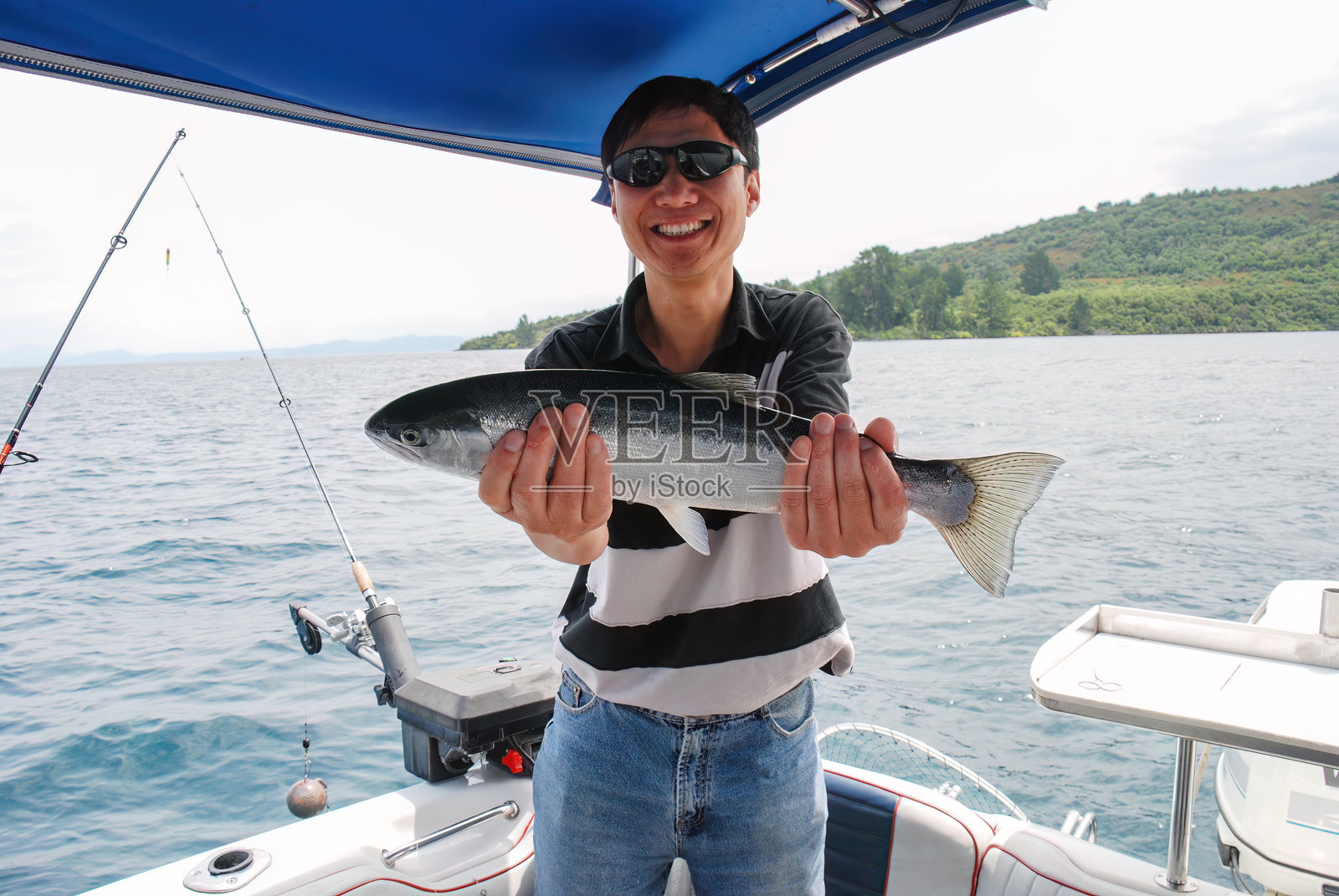 微笑的男子手持捕获的鳟鱼。陶波湖，新西兰。照片摄影图片