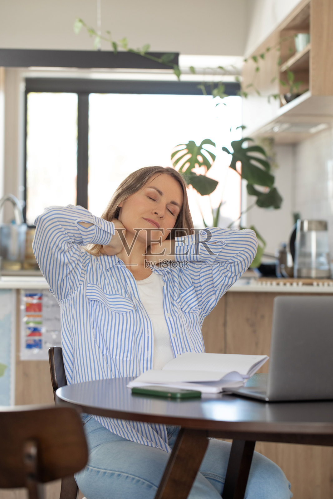 疲惫的女性在使用笔记本电脑时按摩脖子，身边放着计划本照片摄影图片