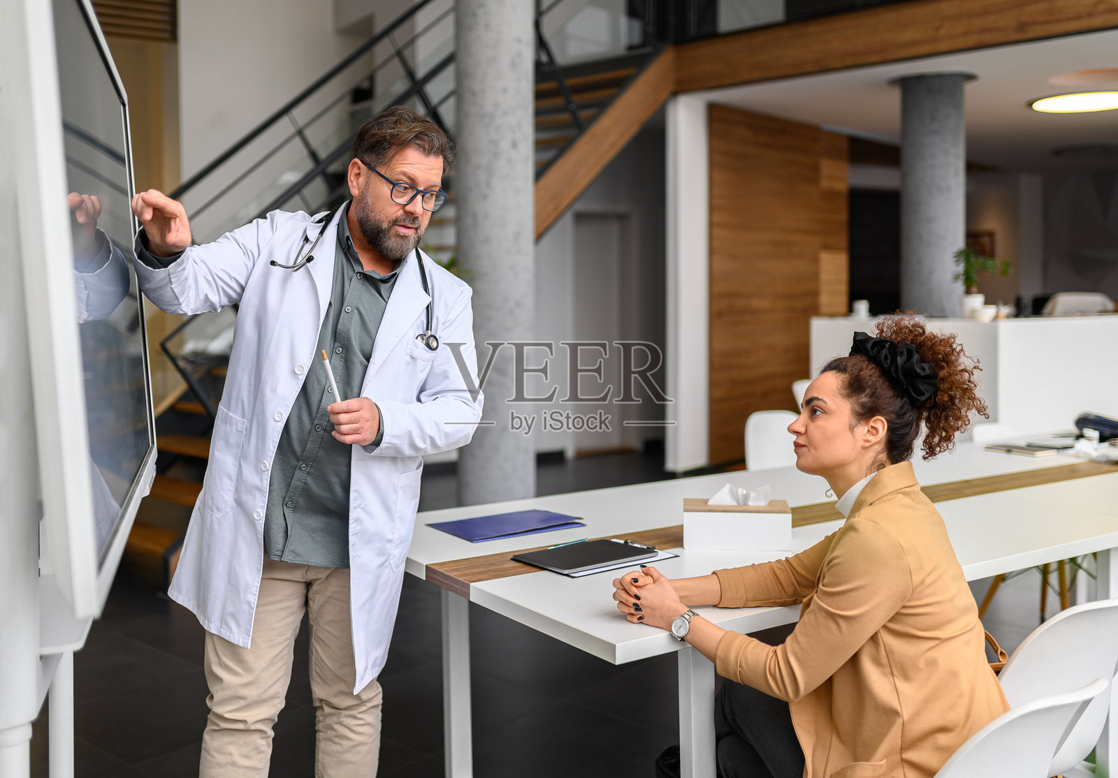 男医生指着电脑屏幕上的X光图像，向女病人解释结果。照片摄影图片