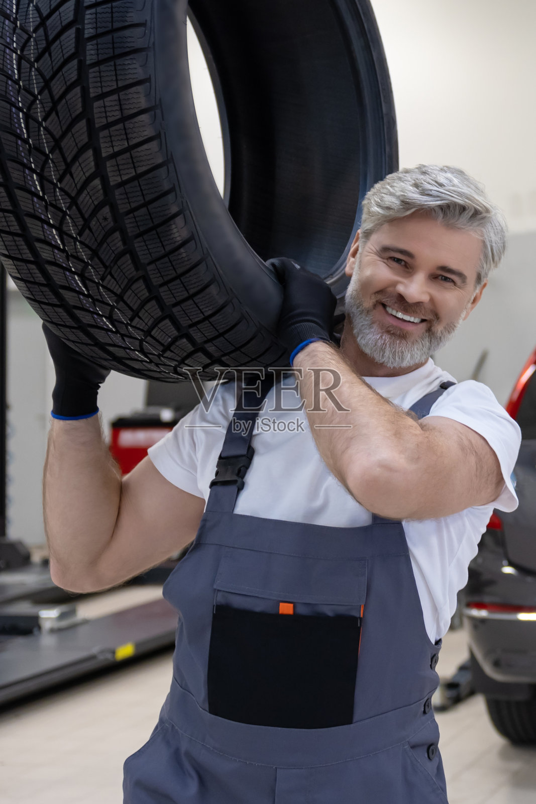 机械师在修理车间更换轮胎，手中拿着轮胎。照片摄影图片