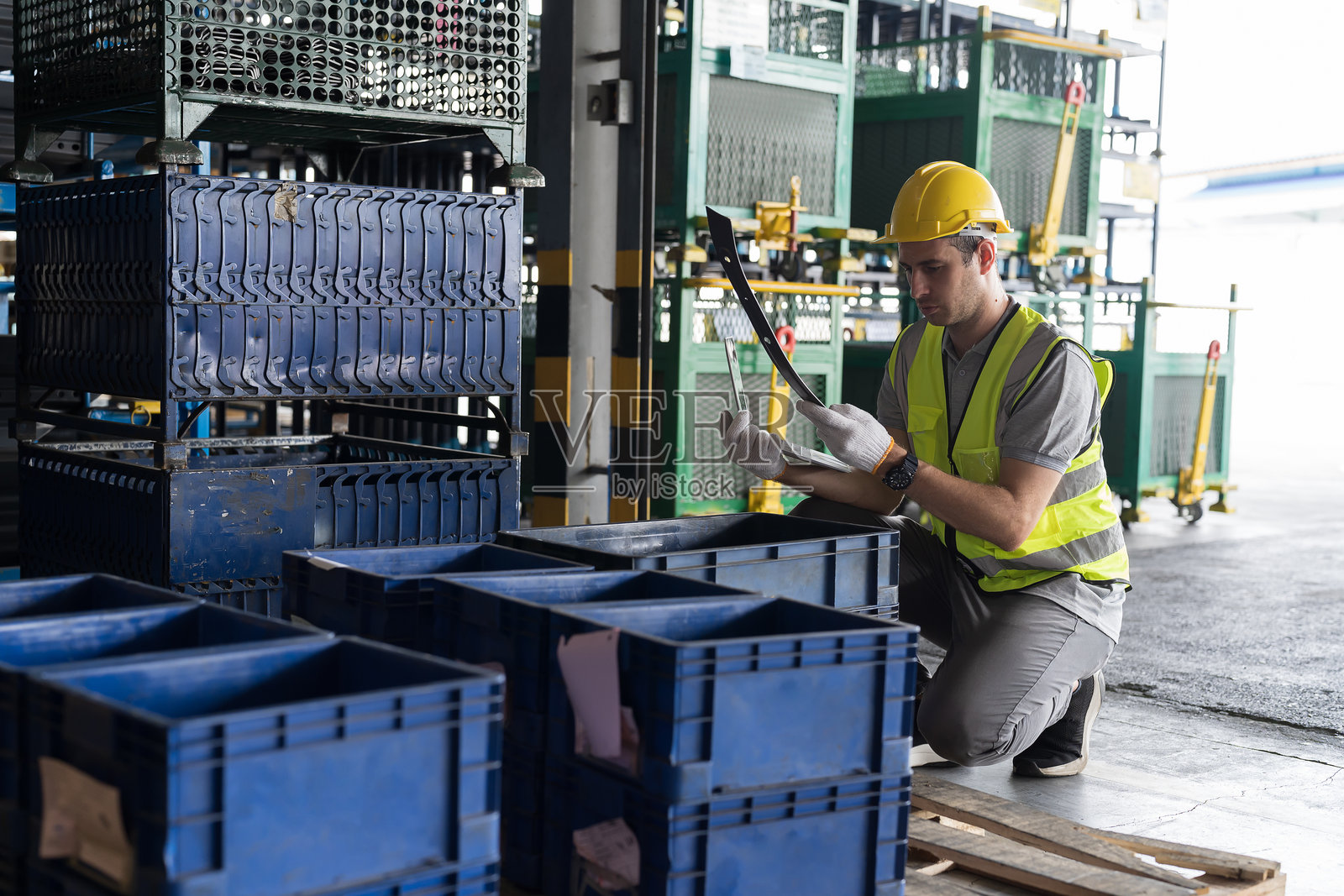 配送仓库，带有电脑的检查清单，男性仓库工人穿着安全制服和头盔，正在使用笔记本电脑检查存储仓库中产品的质量。照片摄影图片