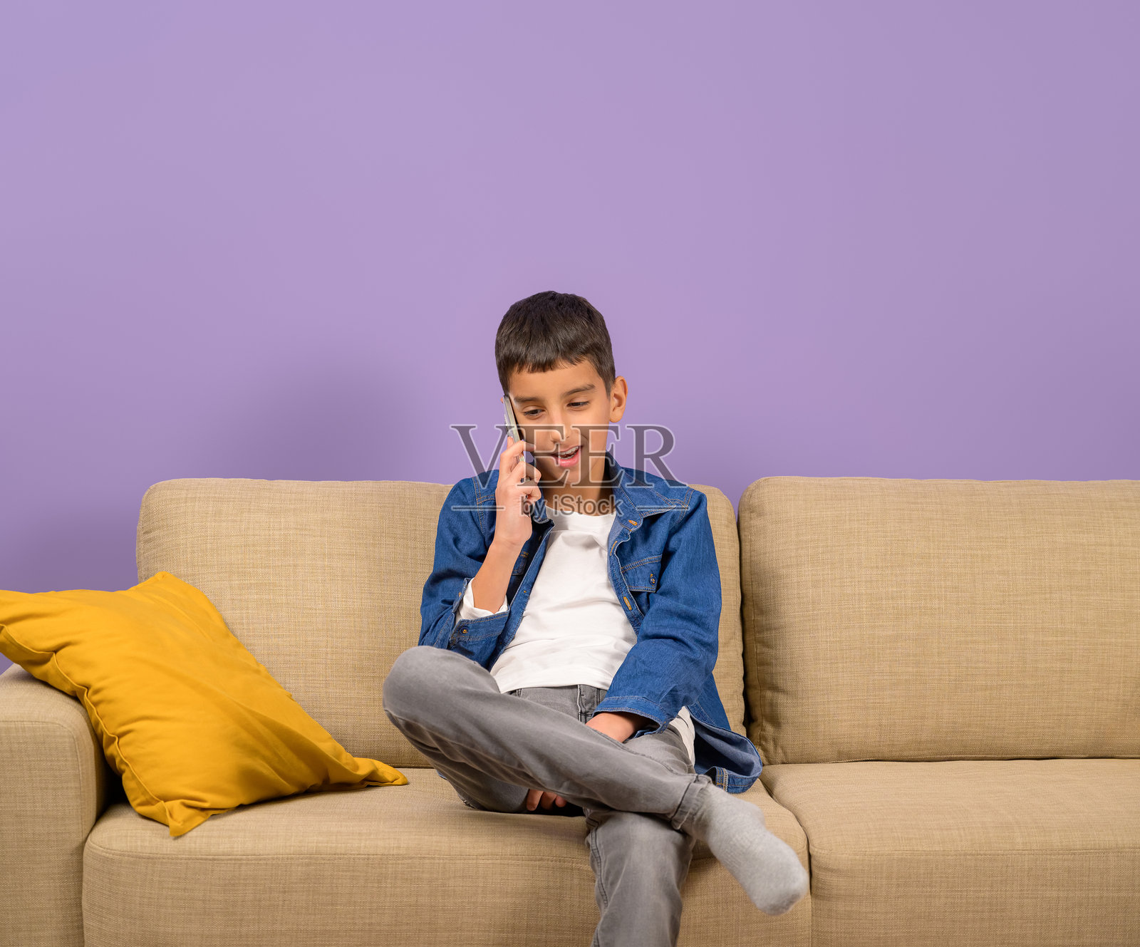 年轻男性企业家坐在沙发上，背景为紫色，正在通过手机讨论。照片摄影图片