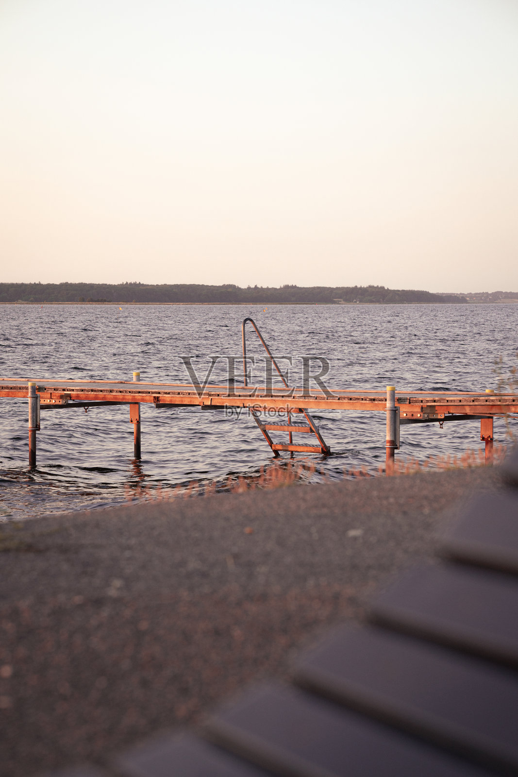 一座木栈道伸向平静的水面，夕阳下柔和的光线在水面上反射。宁静的环境展现了自然风光的美丽。照片摄影图片