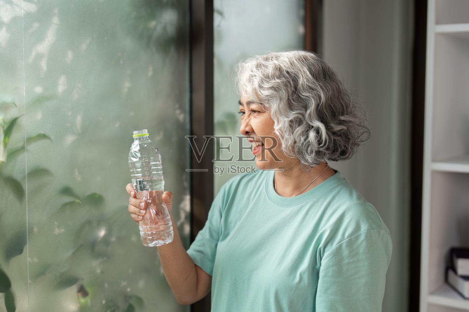 水分补充与健康意识。一位微笑的老年女性手持水瓶，强调水分补充的重要性。照片摄影图片