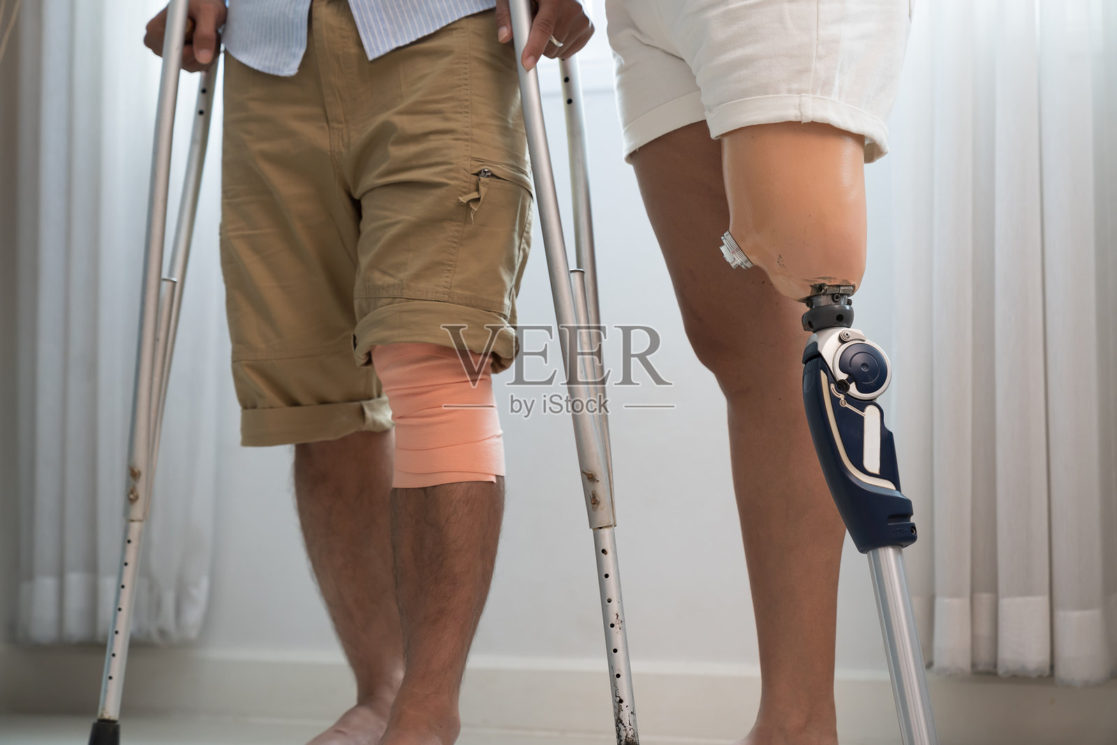 一个膝盖包扎的人和一个使用假肢的人在家里一起用拐杖站着照片摄影图片