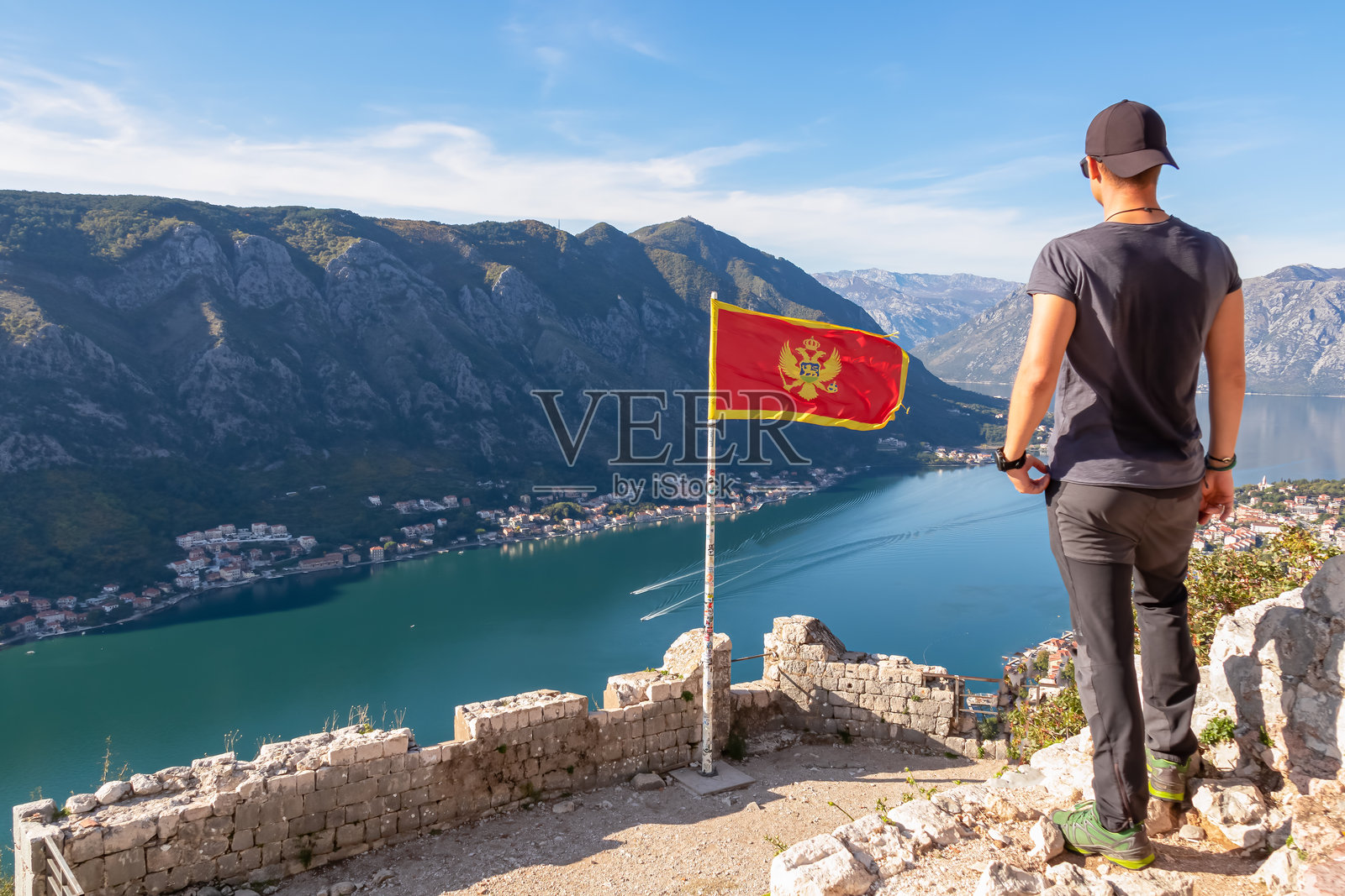 科托尔 - 一名男子在黑山国旗前，迎风而立，背景是科托尔湾圣伊万堡垒的美丽景色照片摄影图片