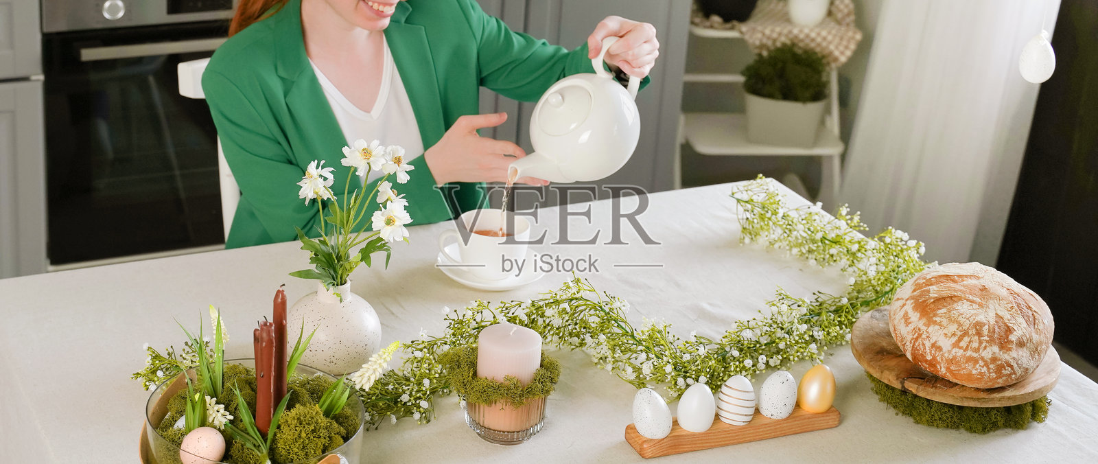 复活节快乐！年轻女性为节日准备了一张摆满复活节糕点、鸡蛋和春季花卉的桌子。照片摄影图片