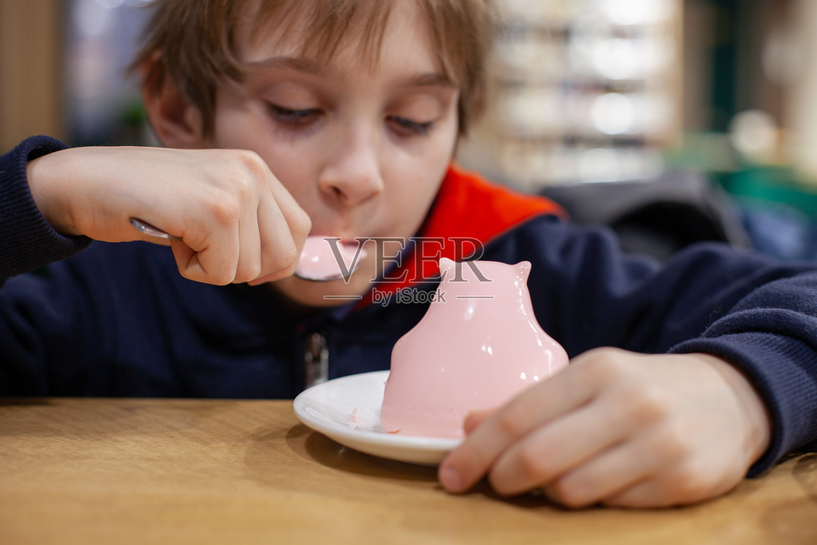 孩子在咖啡馆里用勺子吃粉色的、像水豚形状的果冻甜点。照片摄影图片