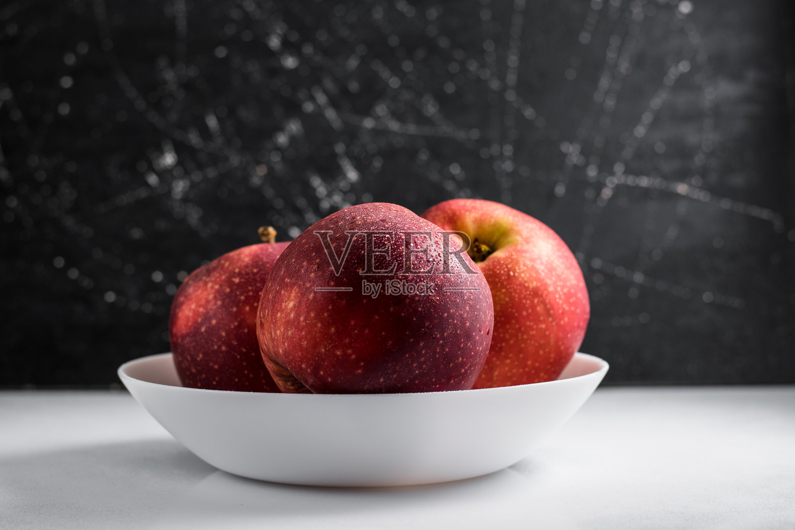 红苹果在水流下闪闪发光，映衬在白色背景上。照片摄影图片