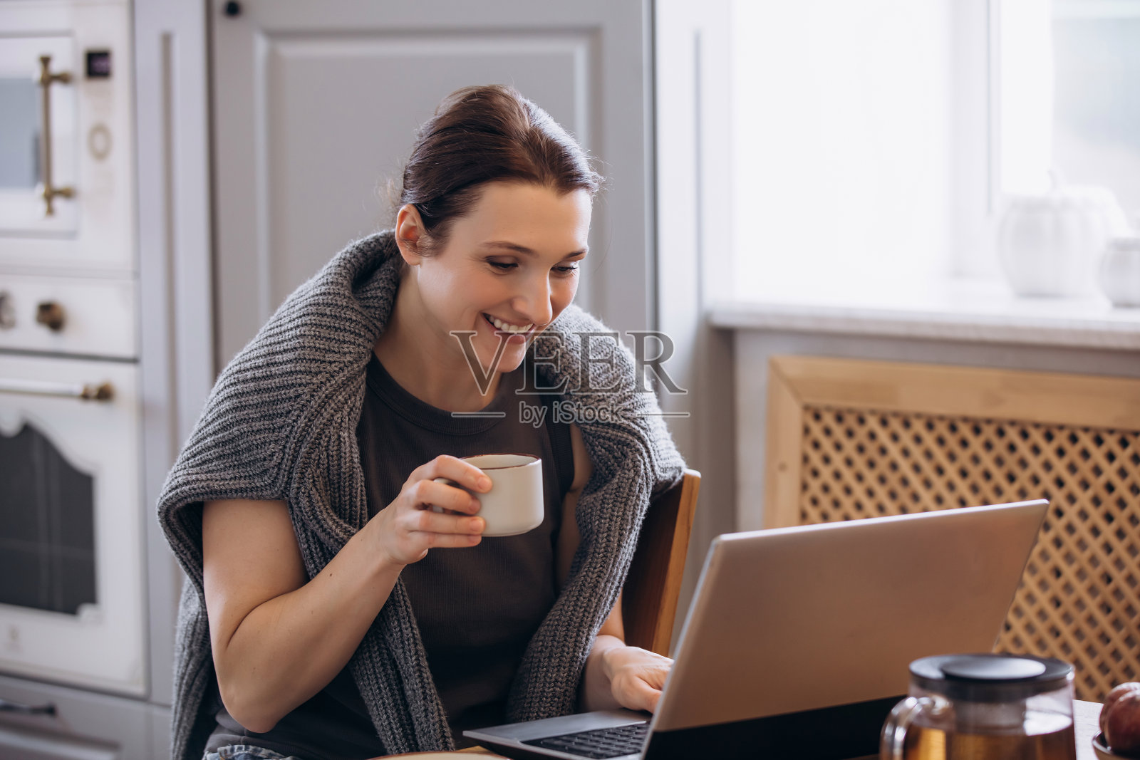 一位美丽的棕发女性在厨房的桌子上使用笔记本电脑。照片摄影图片
