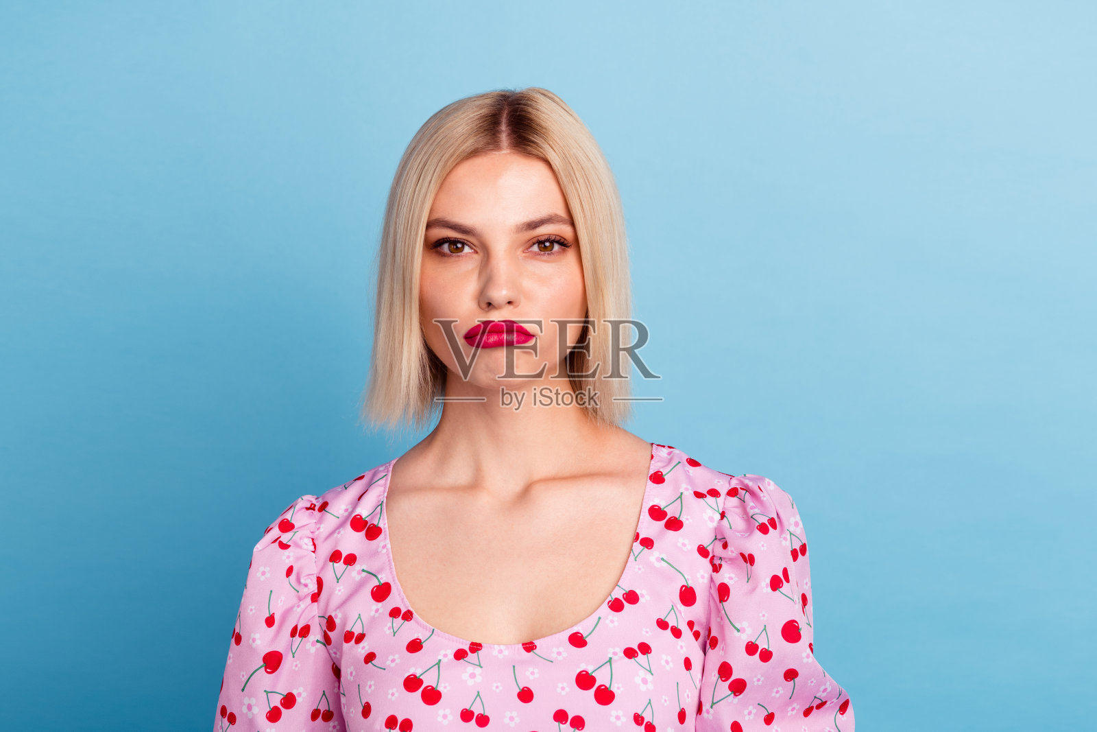 穿着时尚粉色印花衣服的可爱漂亮女孩，心情不好，背景为蓝色。照片摄影图片