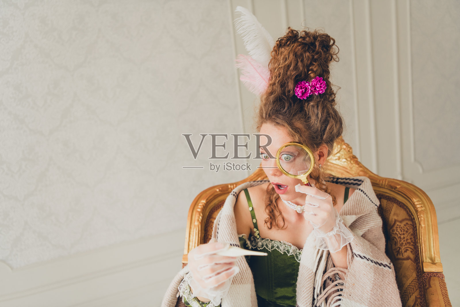 优雅的年轻女性穿着巴洛克风格的服装，在室内用放大镜查看一张纸条照片摄影图片