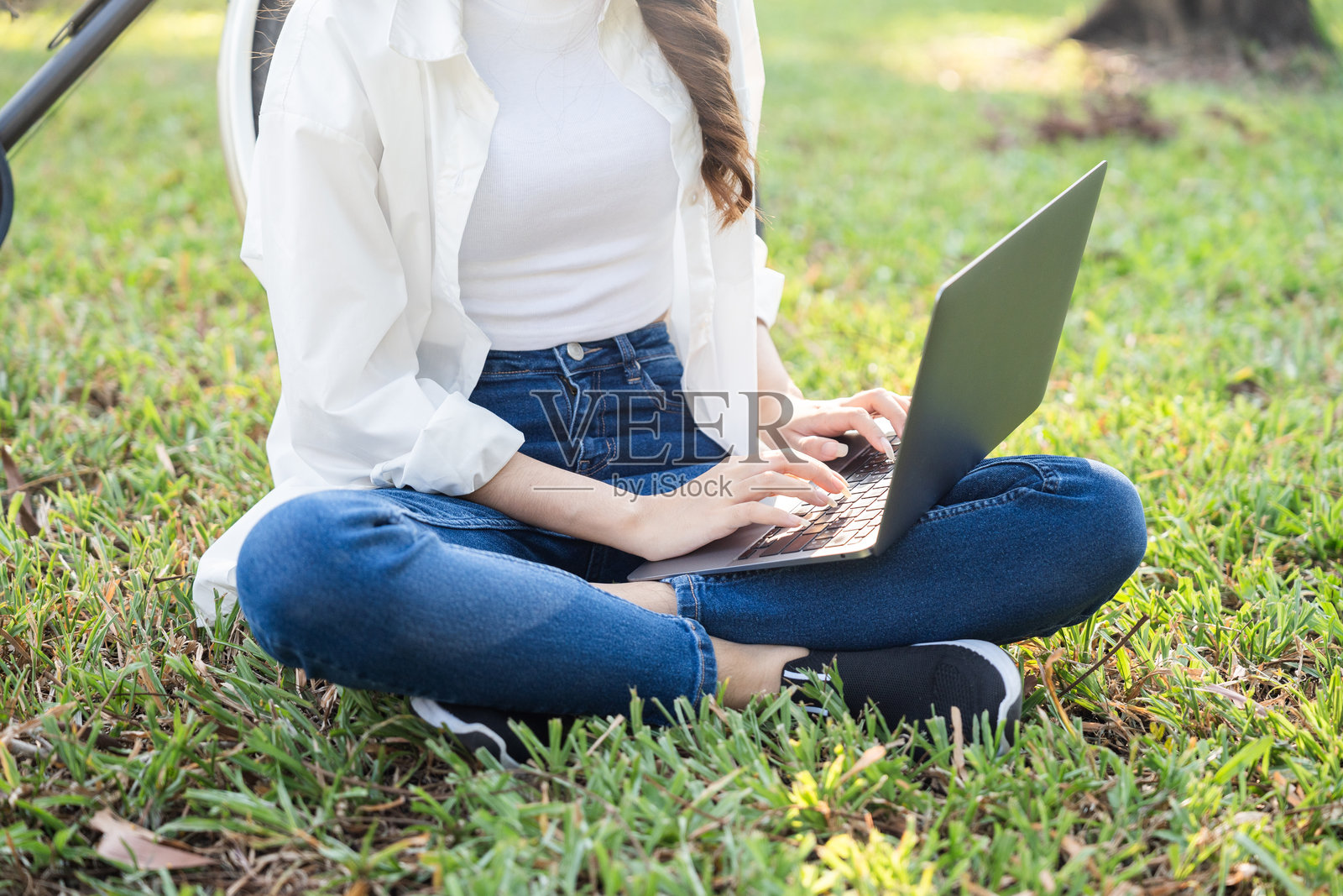 年轻的亚洲青少年在公园里用笔记本电脑学习。夏天，年轻女性在户外工作，享受大自然。人与自然和谐共处。照片摄影图片