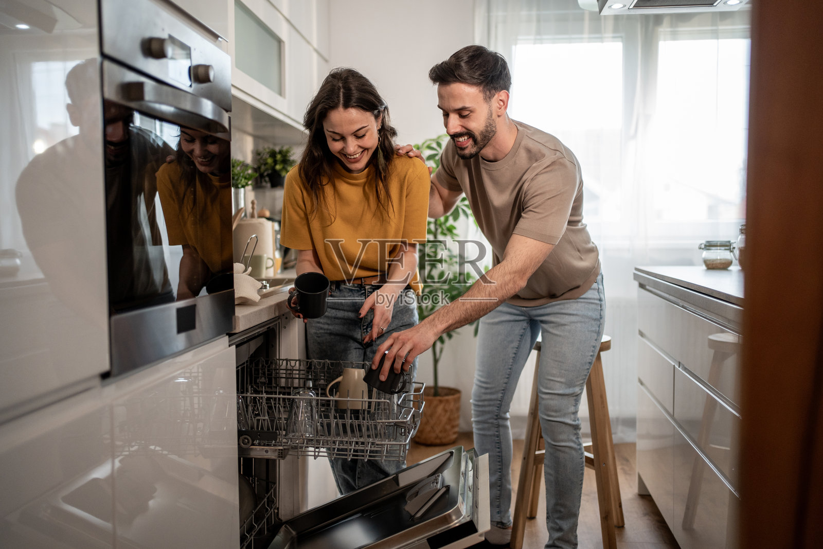 快乐的情侣在现代厨房中从洗碗机里卸下碗碟照片摄影图片
