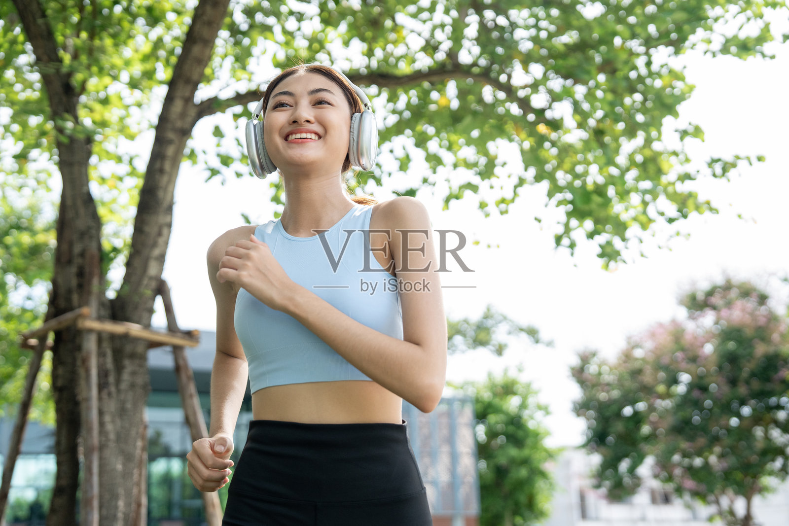 快乐的苗条美丽女性穿着运动服在公园晨跑，伴随着日出。年轻美丽的亚洲女性在户外穿着运动服跑步。早晨锻炼时戴着耳机听音乐。照片摄影图片