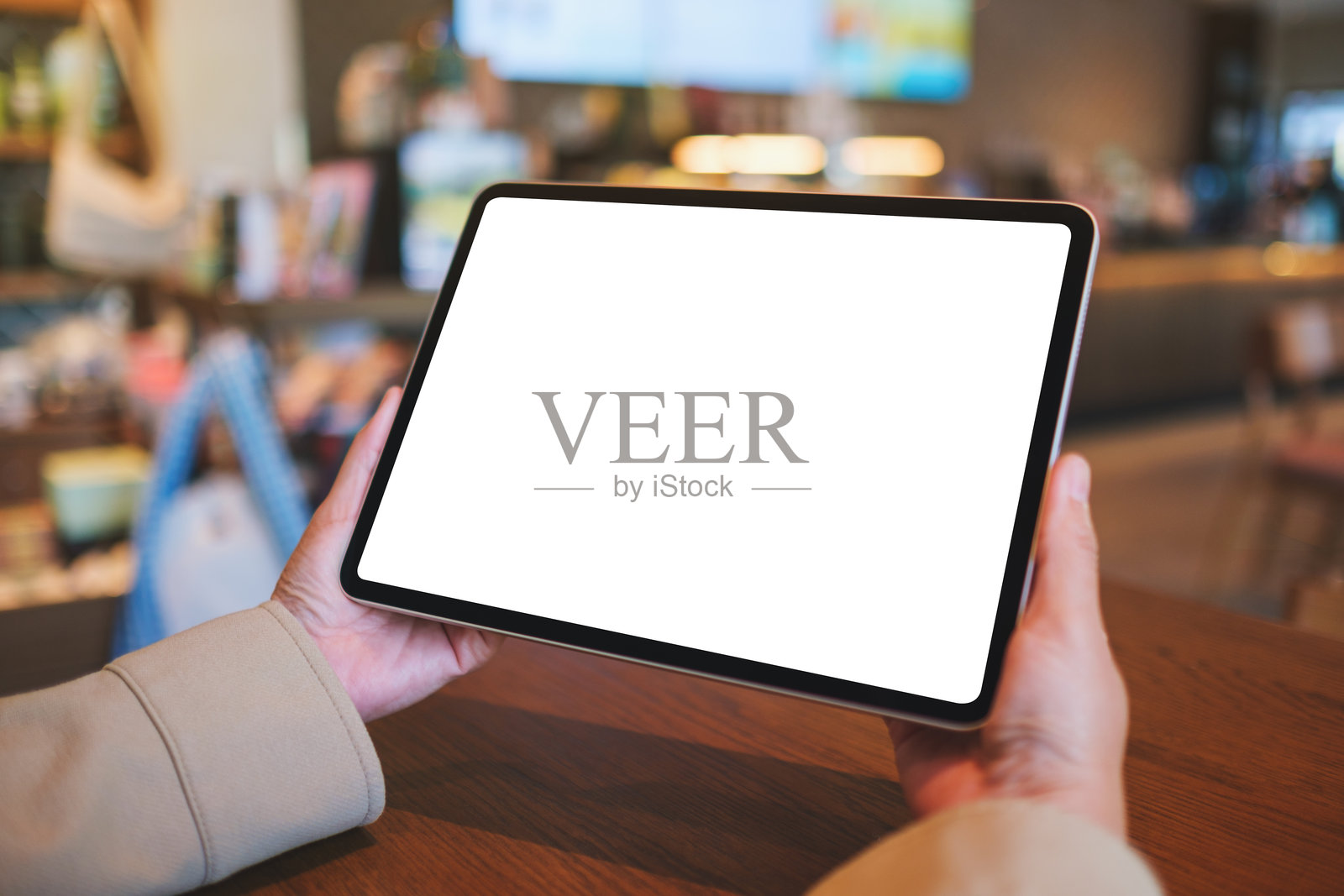 一位女性在咖啡馆里手持数字平板，平板上显示空白的白色桌面屏幕的模型图。照片摄影图片