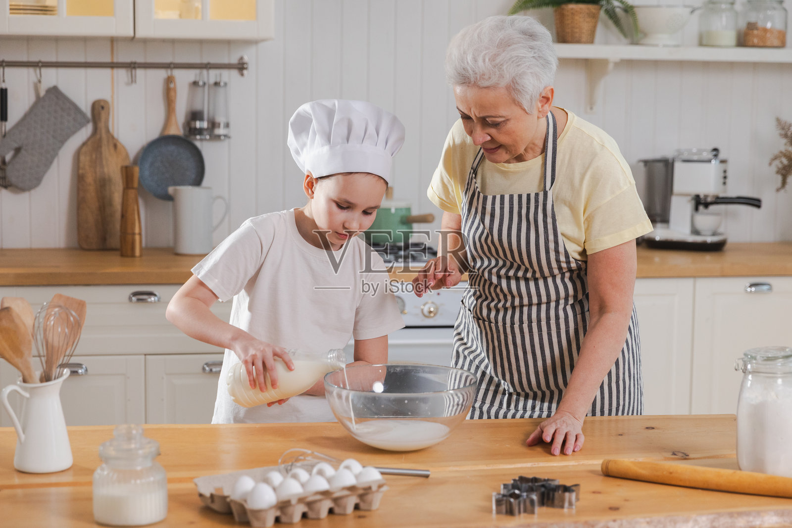 快乐的家庭在厨房。祖母和孙女一起在厨房里做饭。奶奶教小女孩揉面团烤饼干。家庭团队合作，帮助不同代际的家庭概念。照片摄影图片