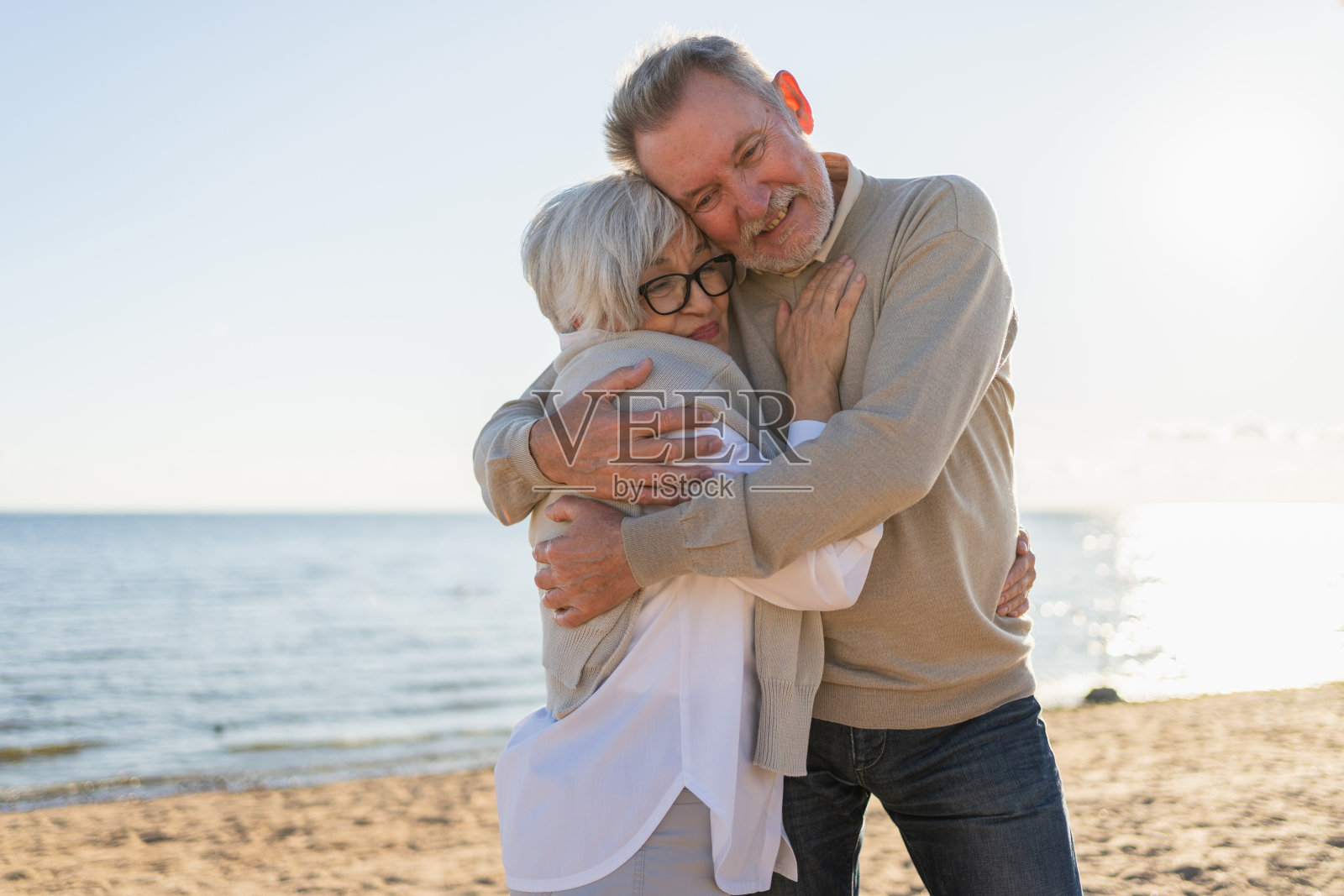 成熟的老年夫妇在海滩上拥抱，享受户外休闲时光。老夫妻温柔地相拥，享受甜蜜的亲密关系。祖父祖母在一起。家庭时刻，充满爱。照片摄影图片