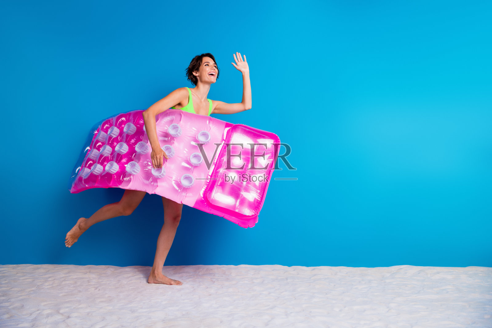 年轻女性穿着色彩鲜艳的泳衣，手持粉色泳池浮具，背景为明亮的蓝色。照片摄影图片