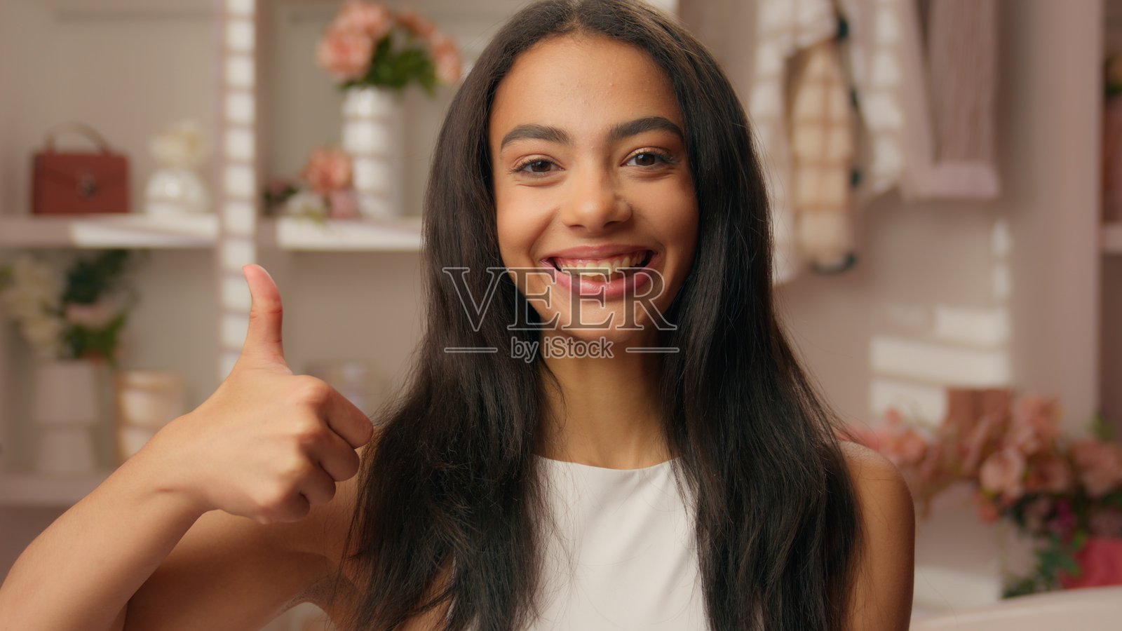 微笑的西班牙裔女孩，健康的女性青少年，在家中酒店的浴室里竖起大拇指，露出灿烂的笑容，推荐美容化妆品和护肤品。照片摄影图片